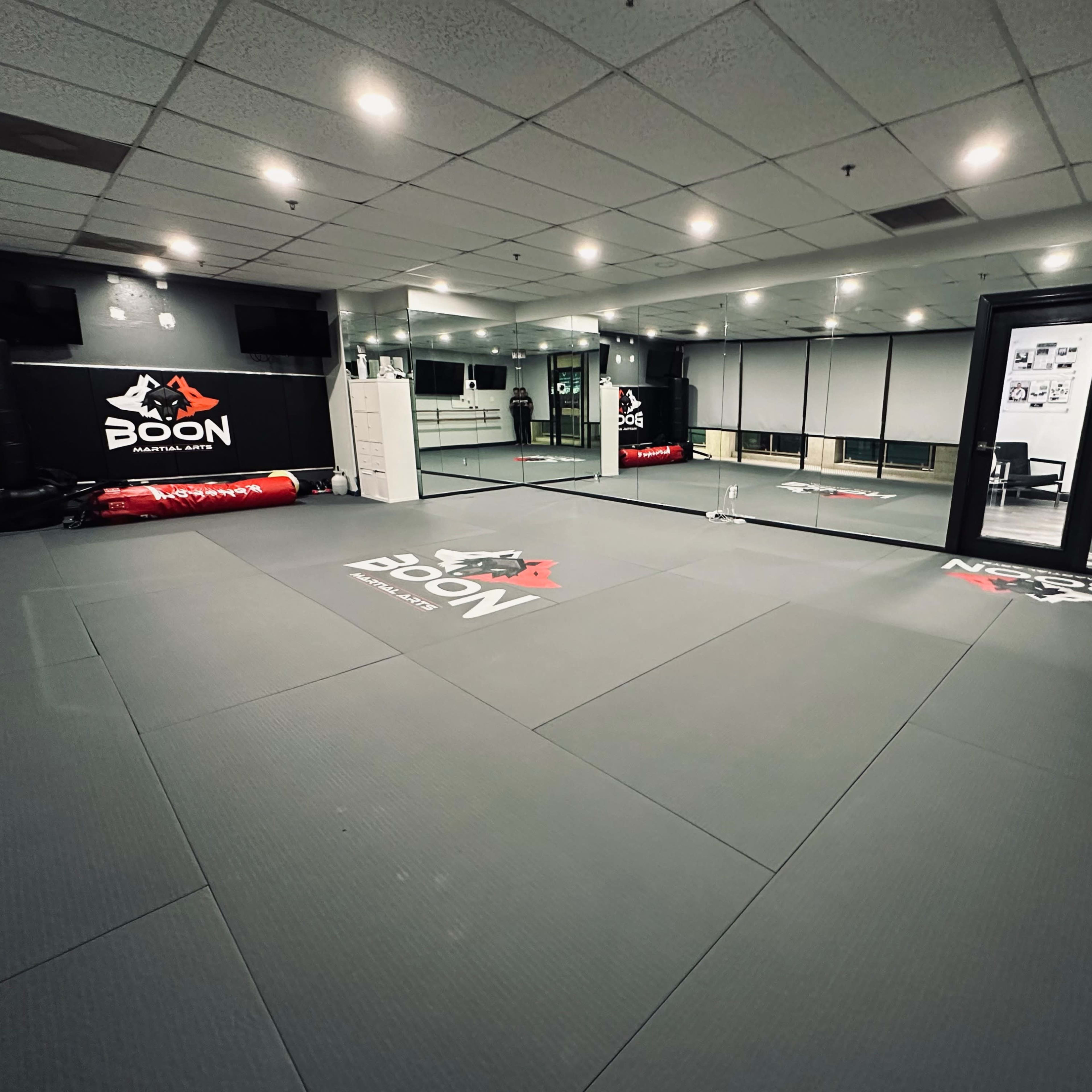 A martial arts training room with padded flooring, mirrors, and a wall featuring the Boon logo.