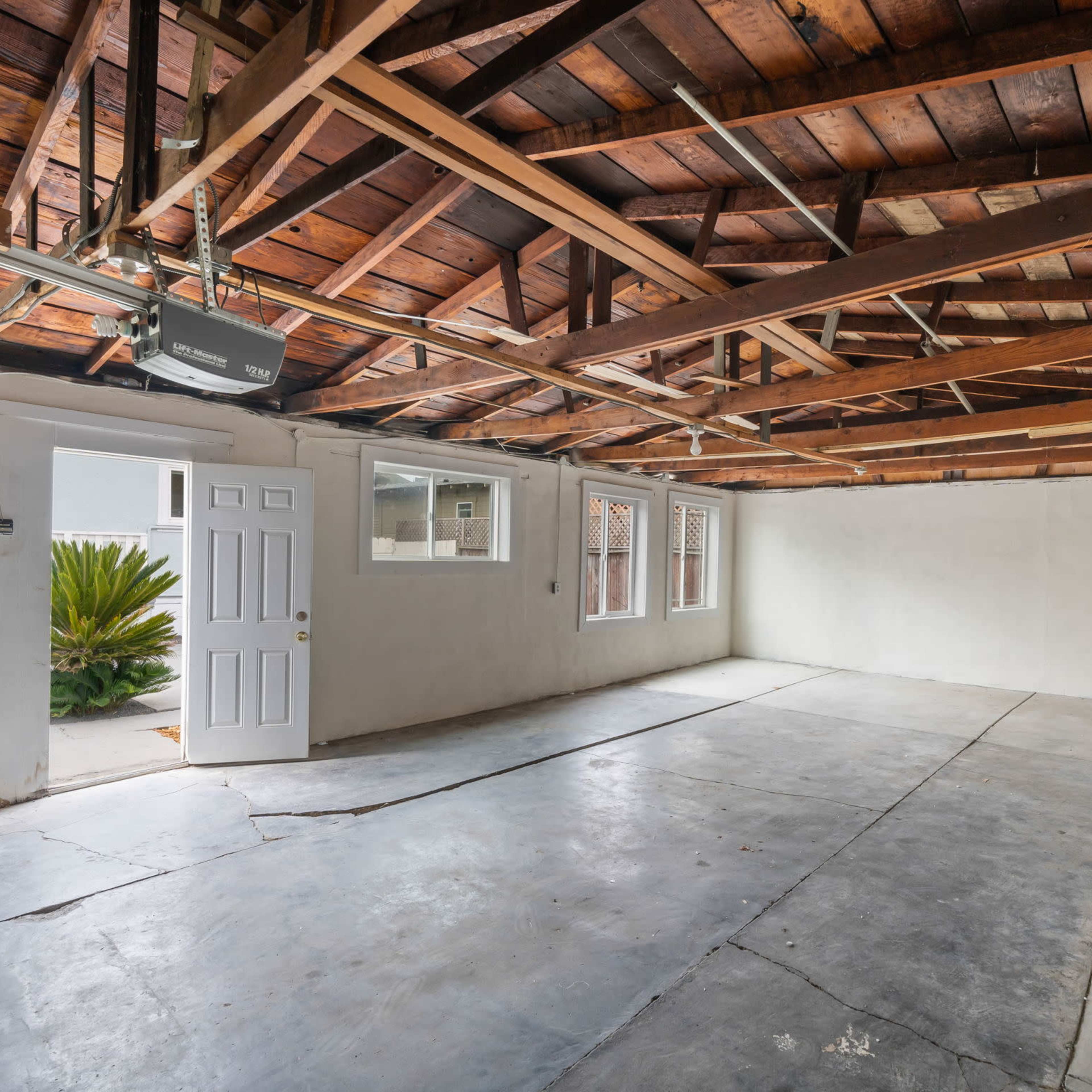 An unfinished room with a concrete floor, exposed wooden beams in the ceiling, and a door leading to an outdoor area.