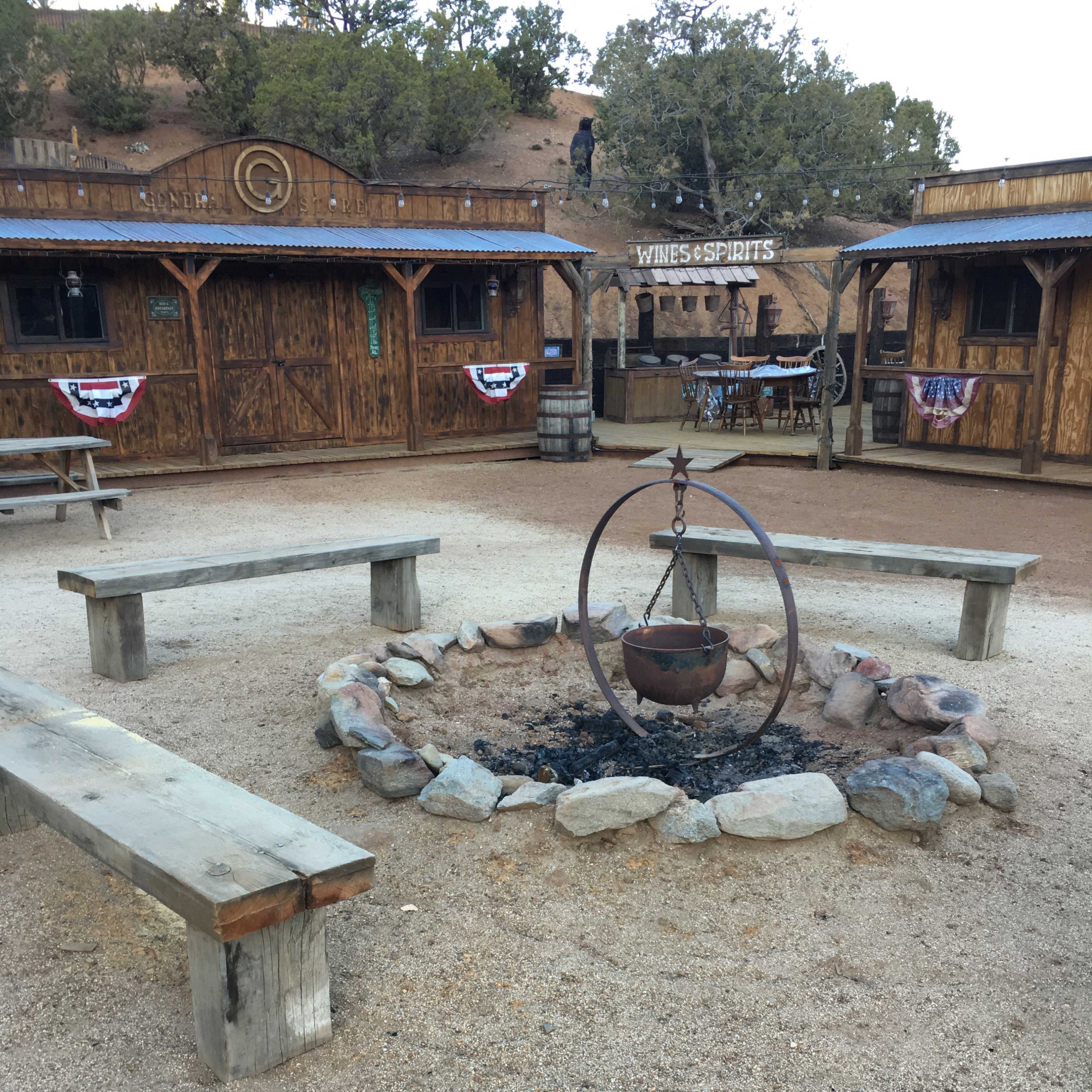 A circular fire pit surrounded by wooden benches in a rustic outdoor setting with wooden structures in the background.