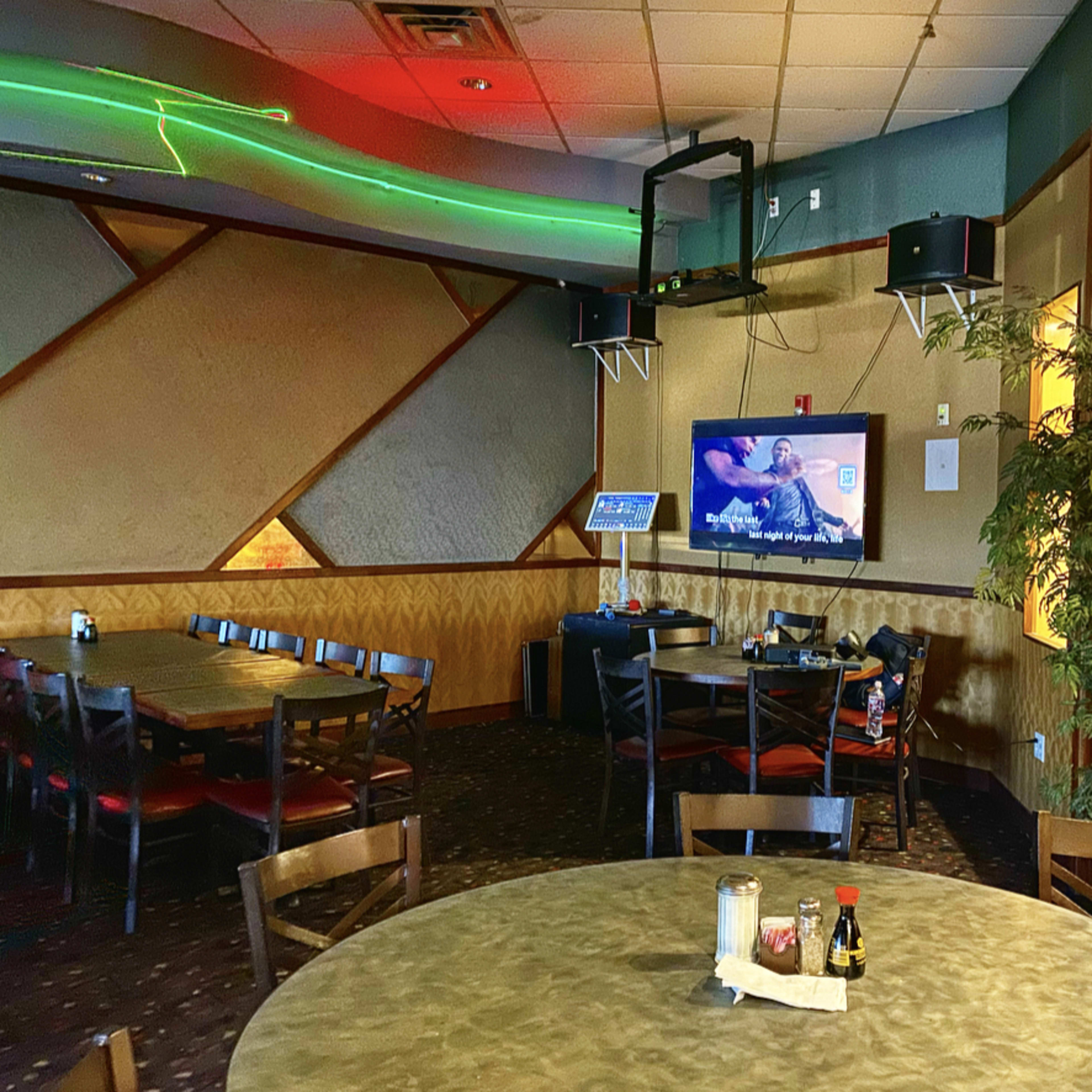 A dining area with tables and chairs, a television mounted on the wall, and a potted plant in the corner.