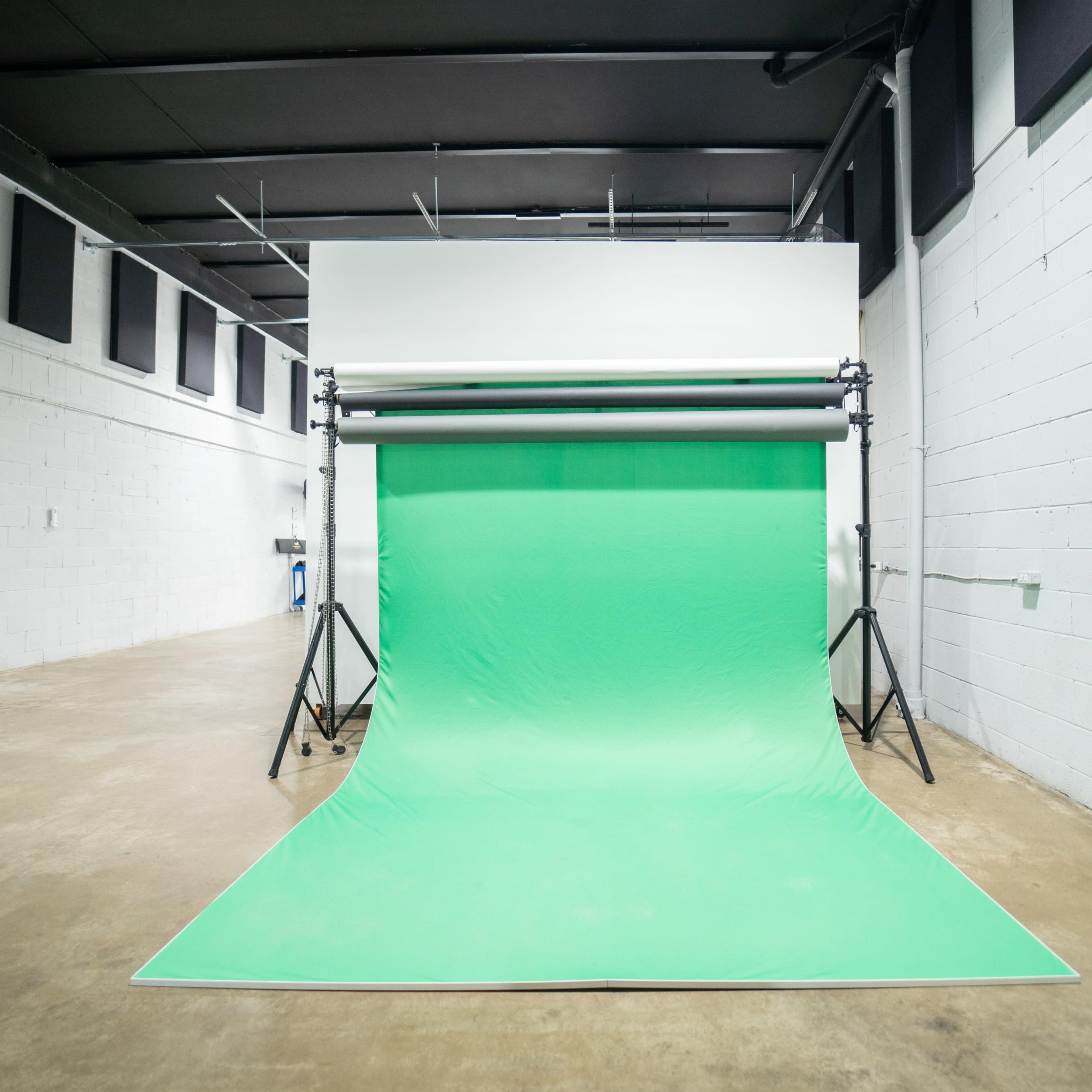 A studio space featuring a green screen setup against a plain concrete wall.