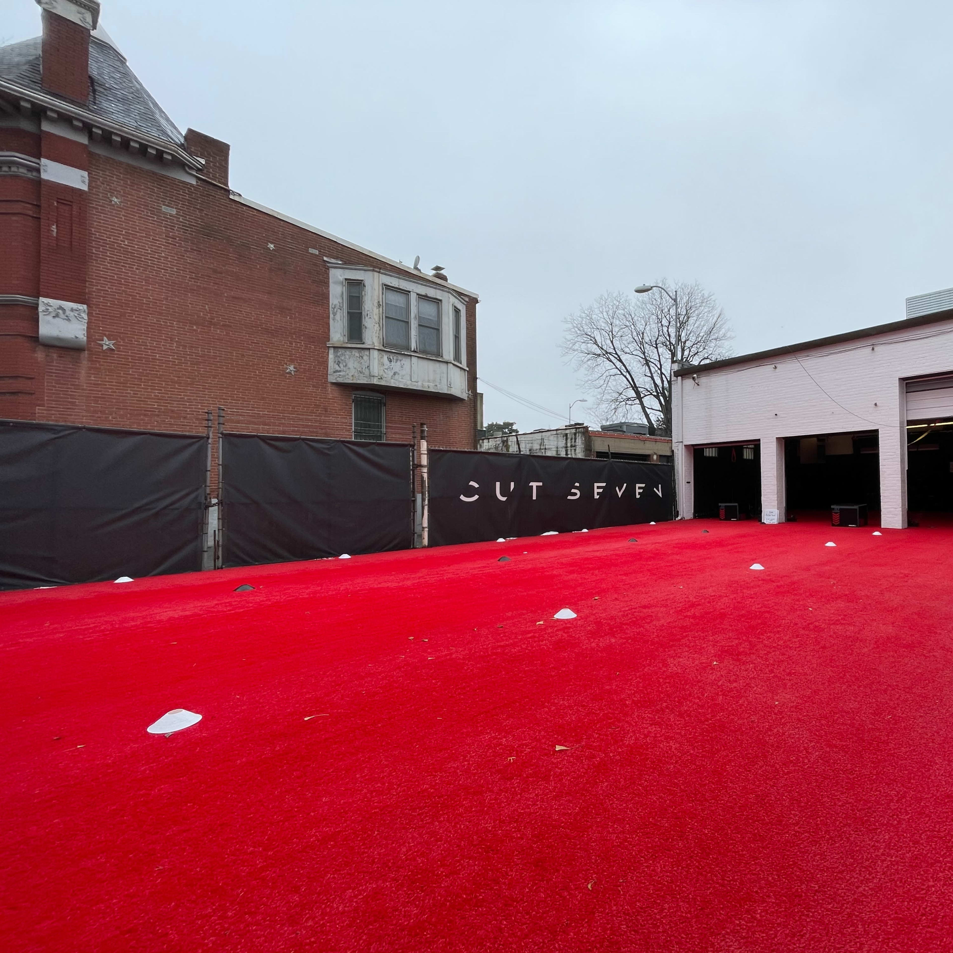 A red carpeted area in an outdoor space behind a building, with a black fence surrounding it.