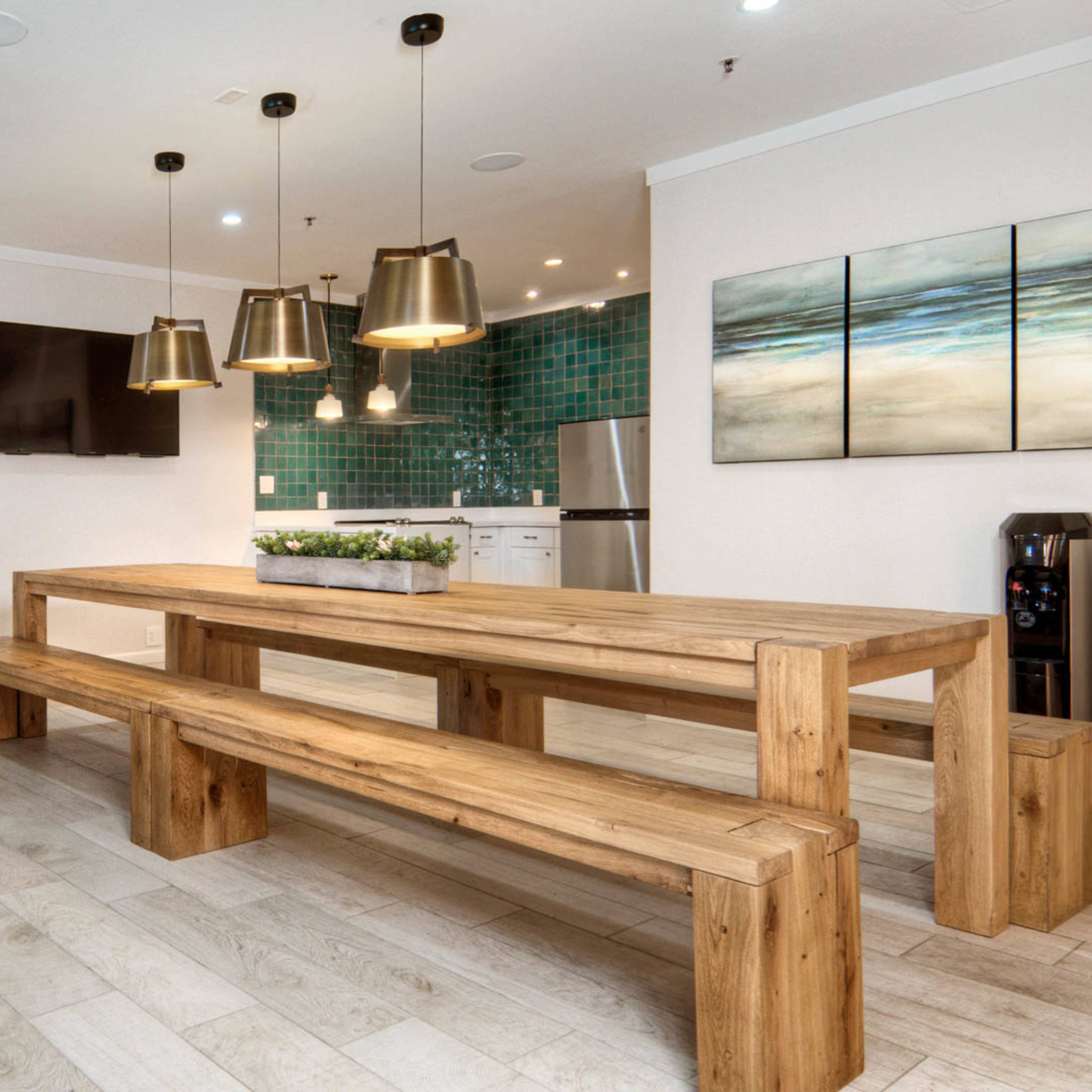A modern dining area features a large wooden table with benches, surrounded by green upholstered chairs, and a kitchen area with teal tile in the background.