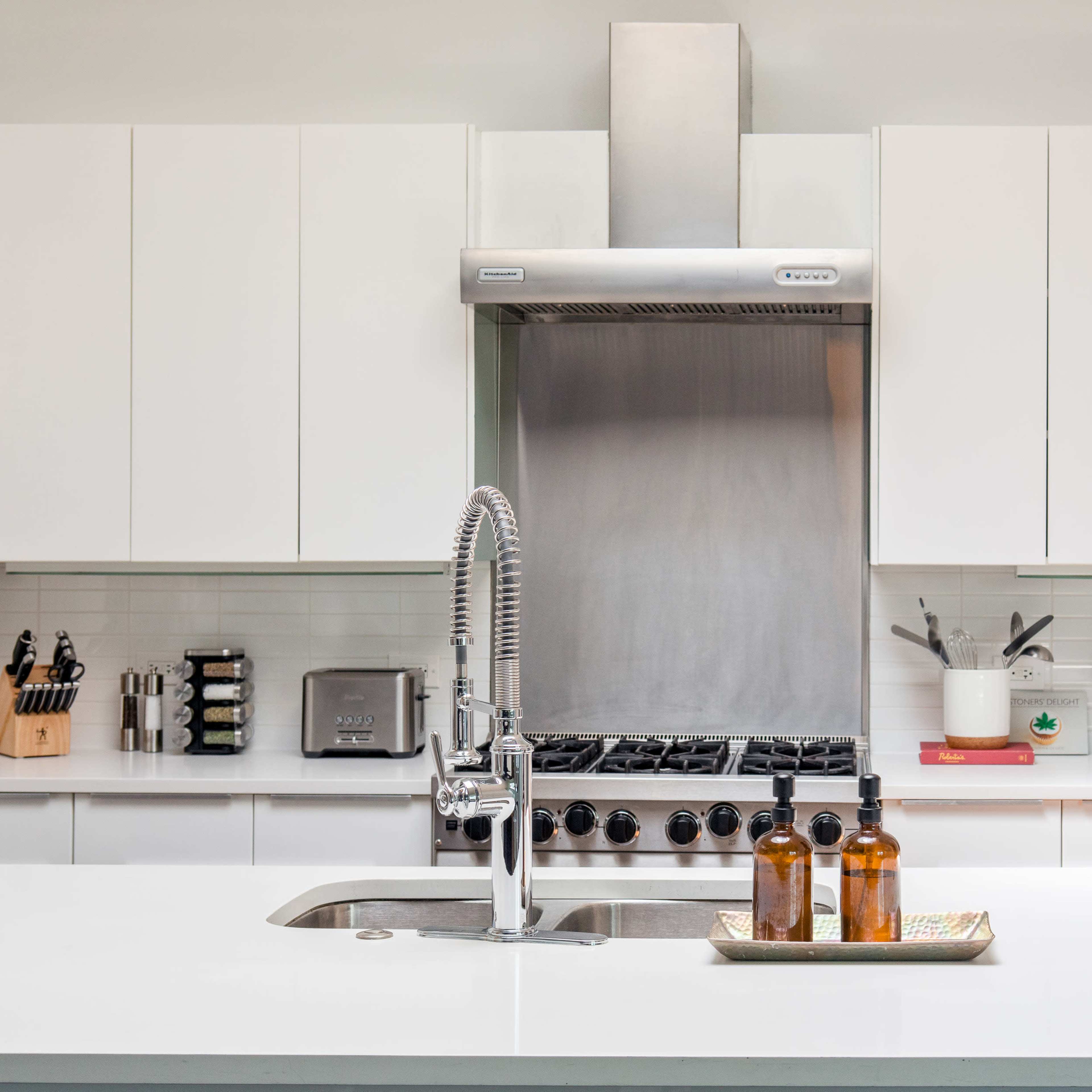 A modern kitchen features stainless steel appliances, white cabinetry, and a central island with a sink and countertop items.
