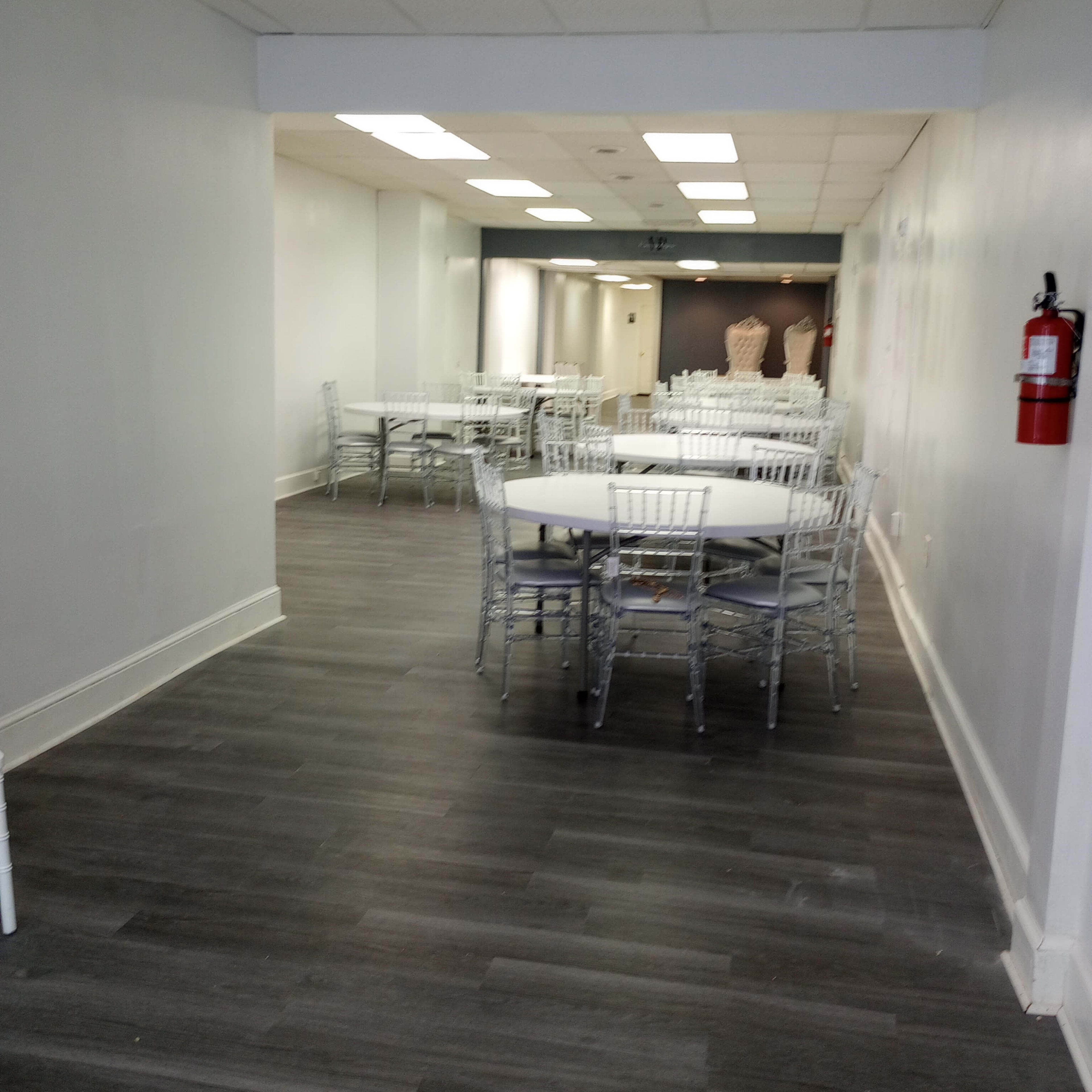 A long, narrow room with several tables and chairs arranged throughout, featuring a clean, modern design and muted colors.