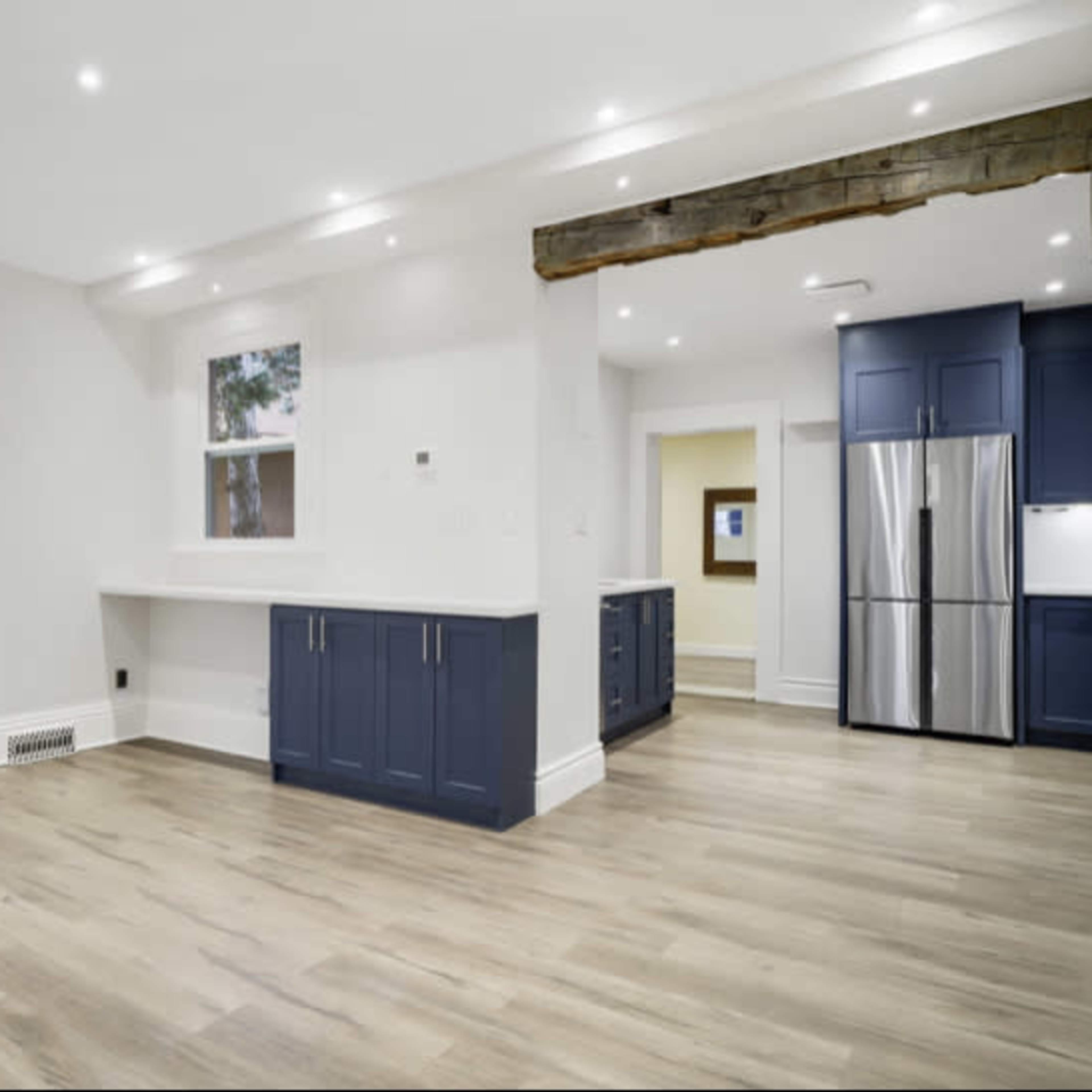 A modern kitchen interior with light wood flooring, blue cabinetry, and stainless steel appliances.