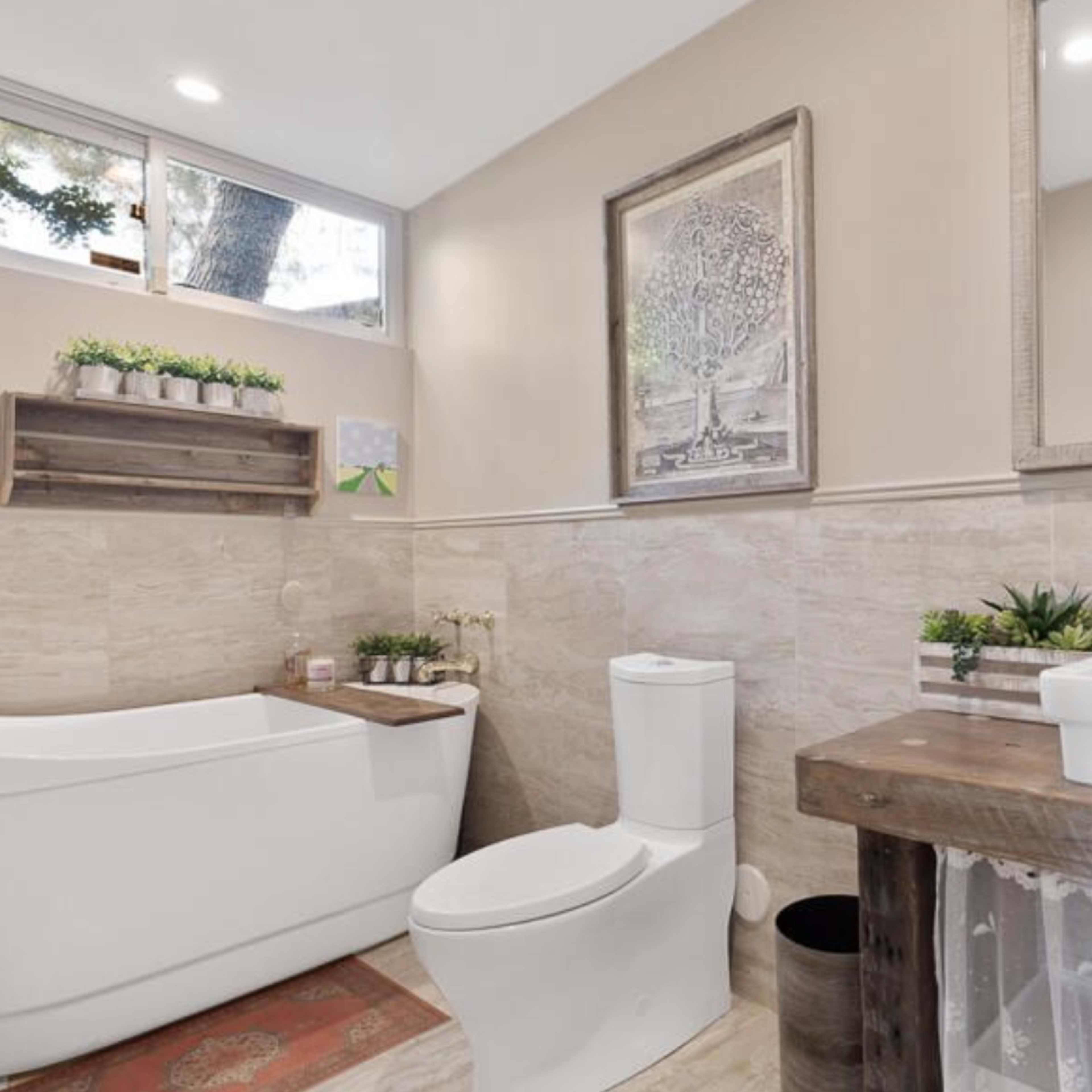 A modern bathroom featuring a freestanding bathtub, a white toilet, a wooden sink vanity, and decorative plants on shelves.