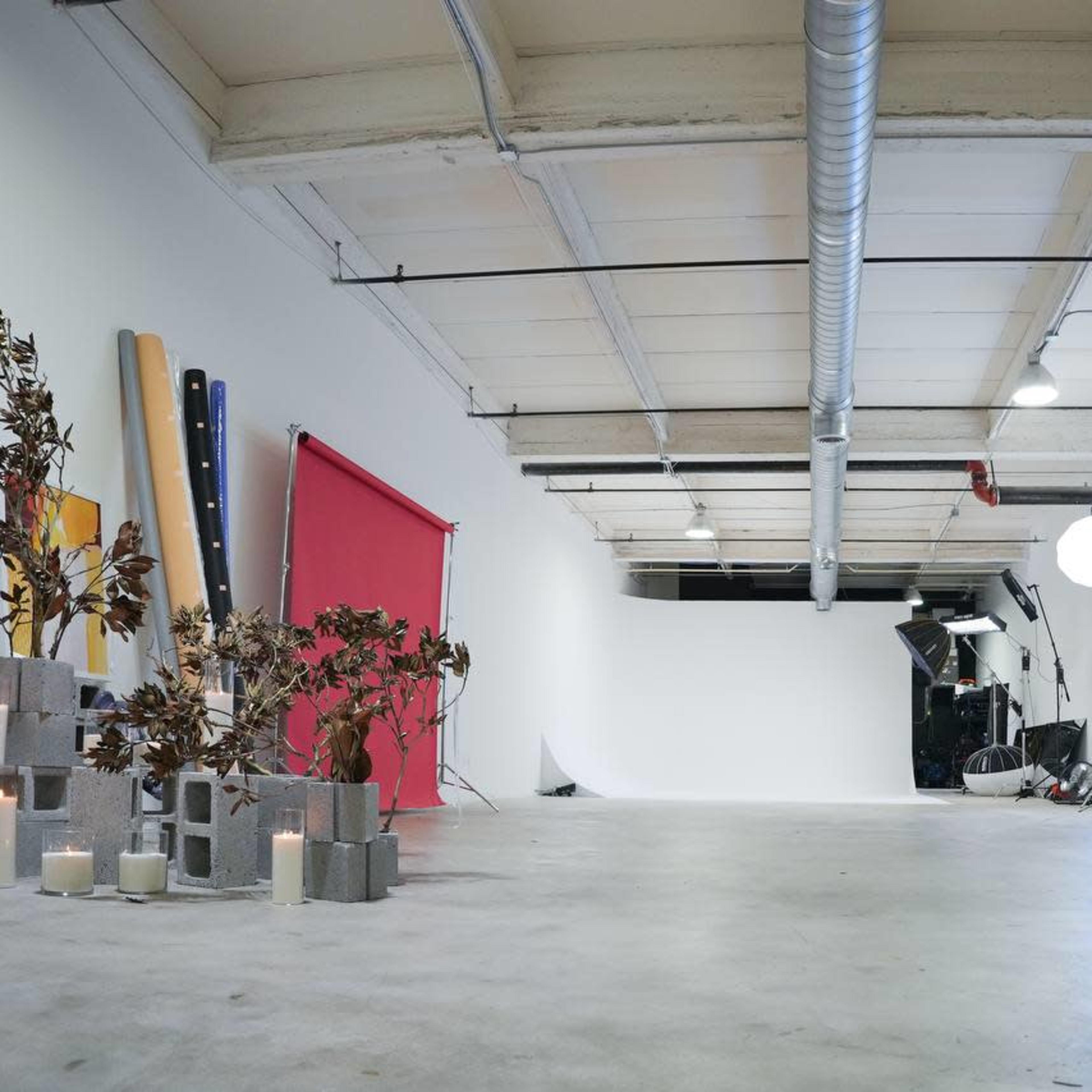 A spacious studio with a red backdrop, various equipment, and decorative plants arranged on one side.