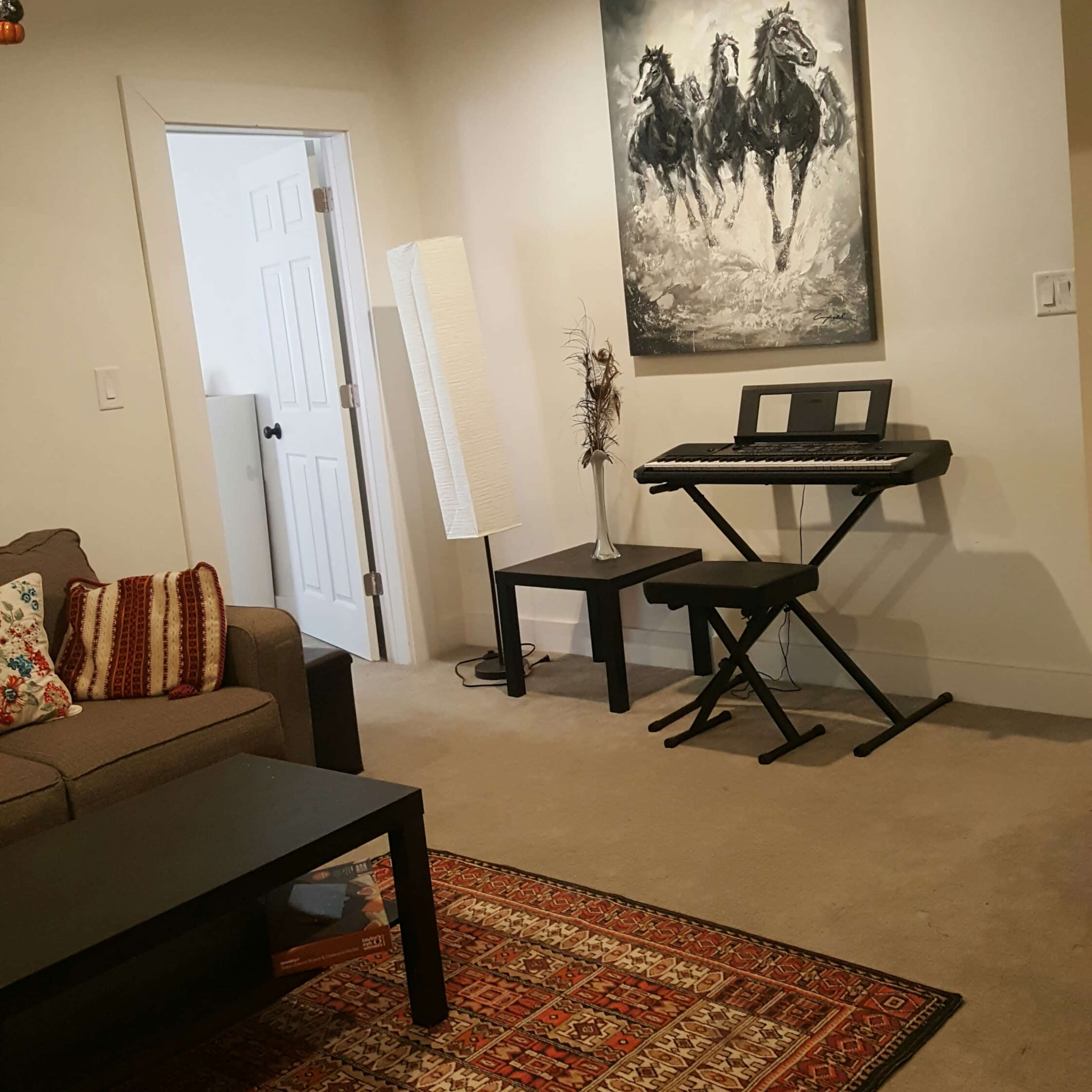 A living room with a gray sofa, a dark coffee table, a keyboard on a stand, and a large painting of three horses on the wall.