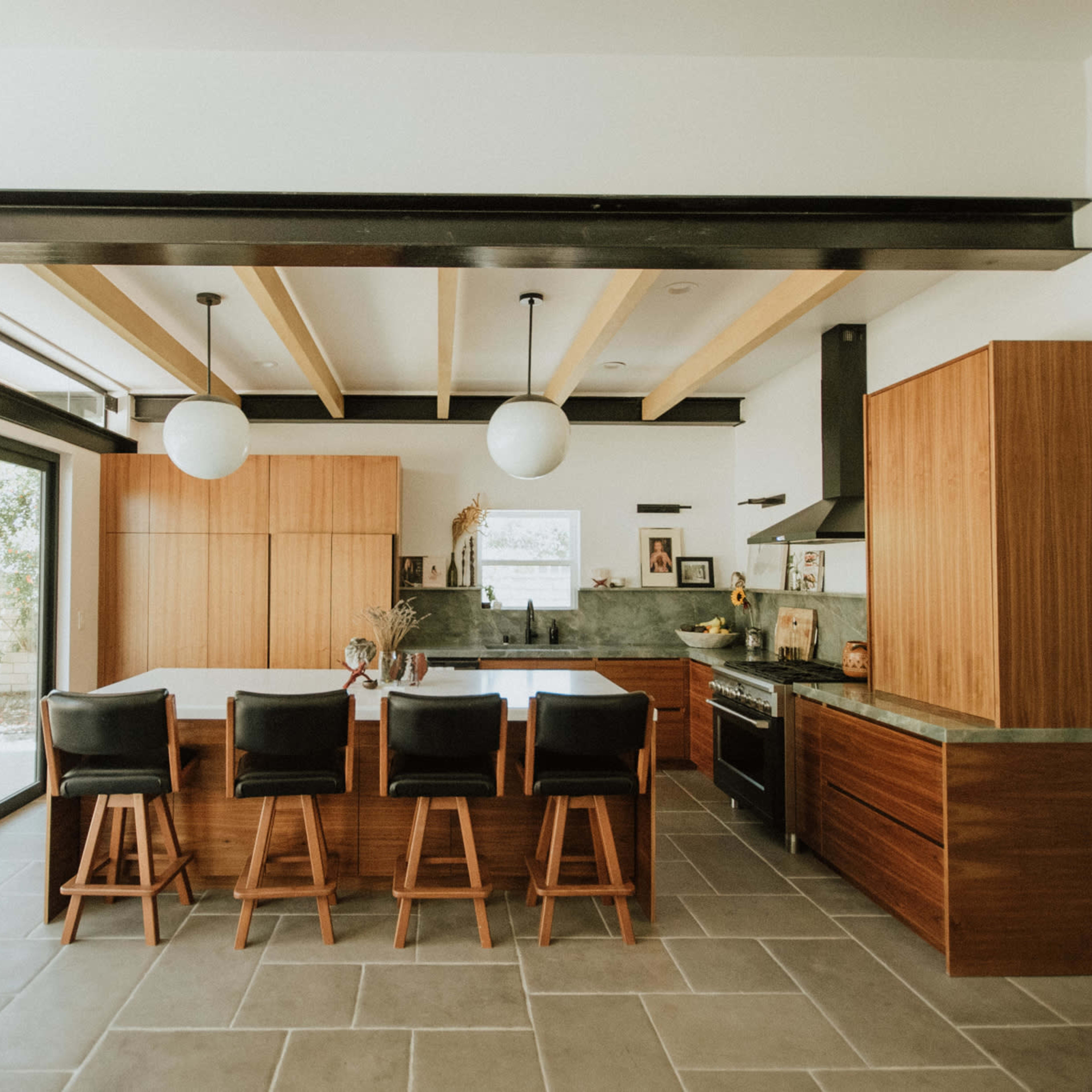 A modern kitchen features wooden cabinetry, a large island with bar seating, and large windows allowing natural light.