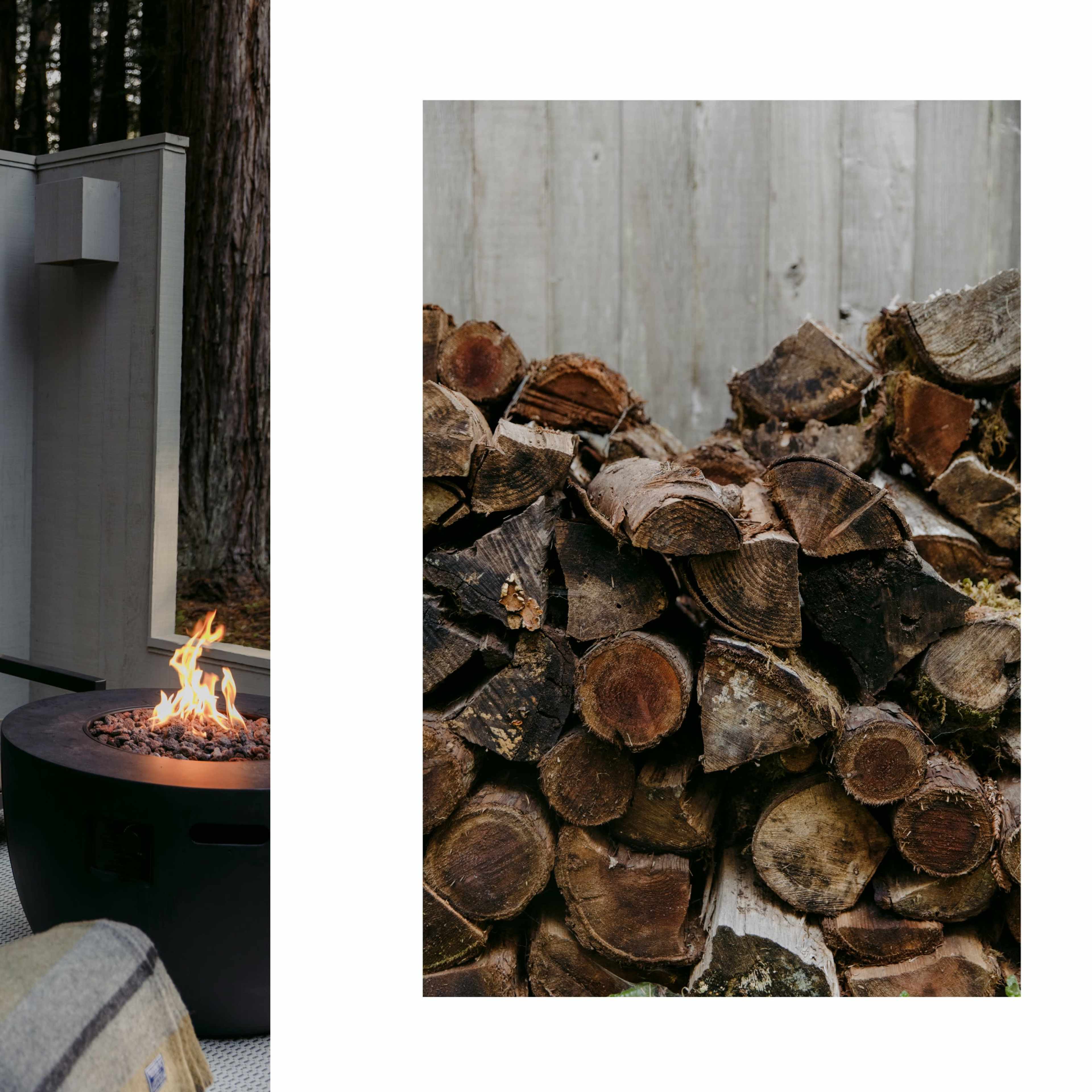 A cozy outdoor seating area with a fire pit surrounded by tall trees and a neatly stacked pile of firewood nearby.