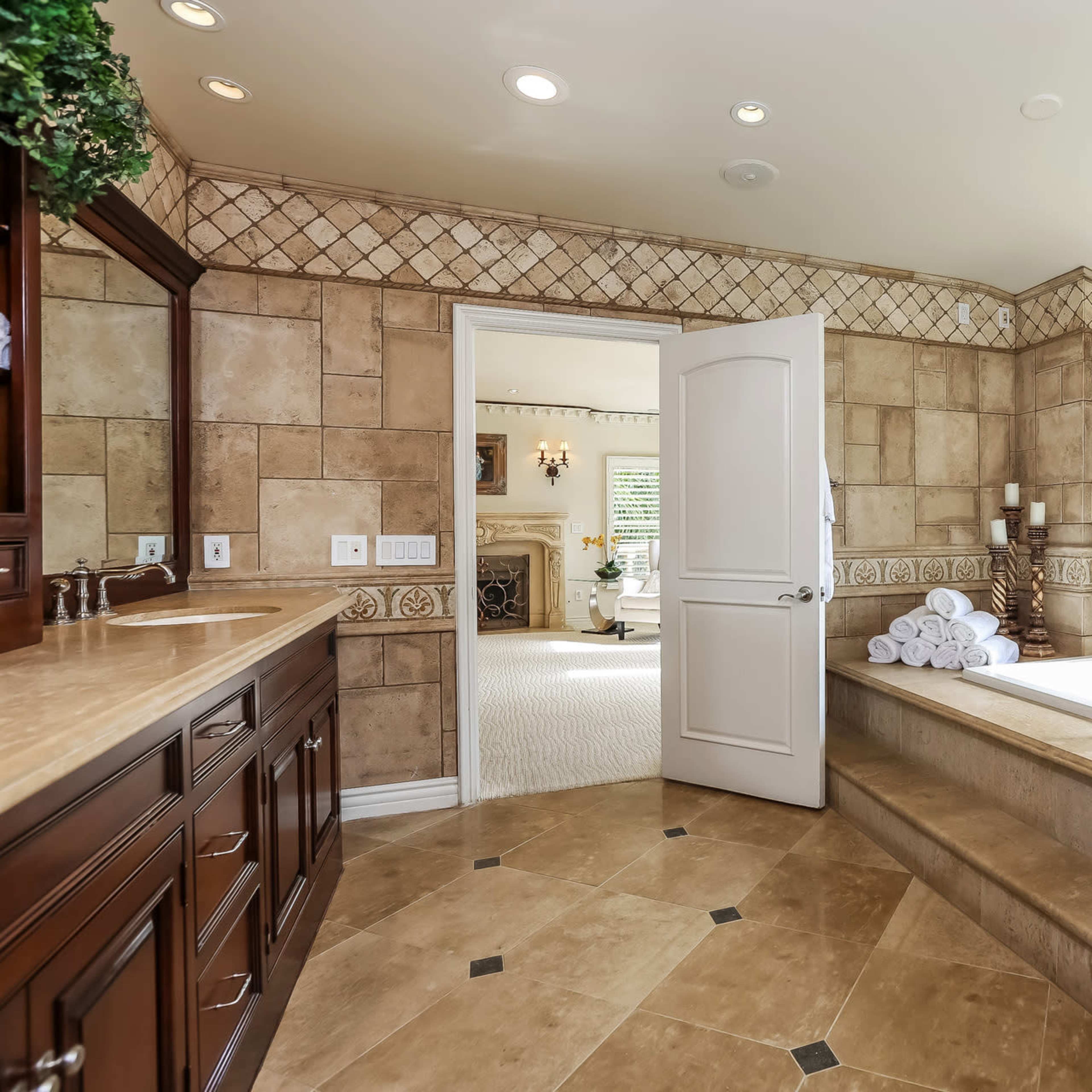 A spacious bathroom features a large tub positioned under a window with a view, surrounded by tiled walls and a dual sink vanity.