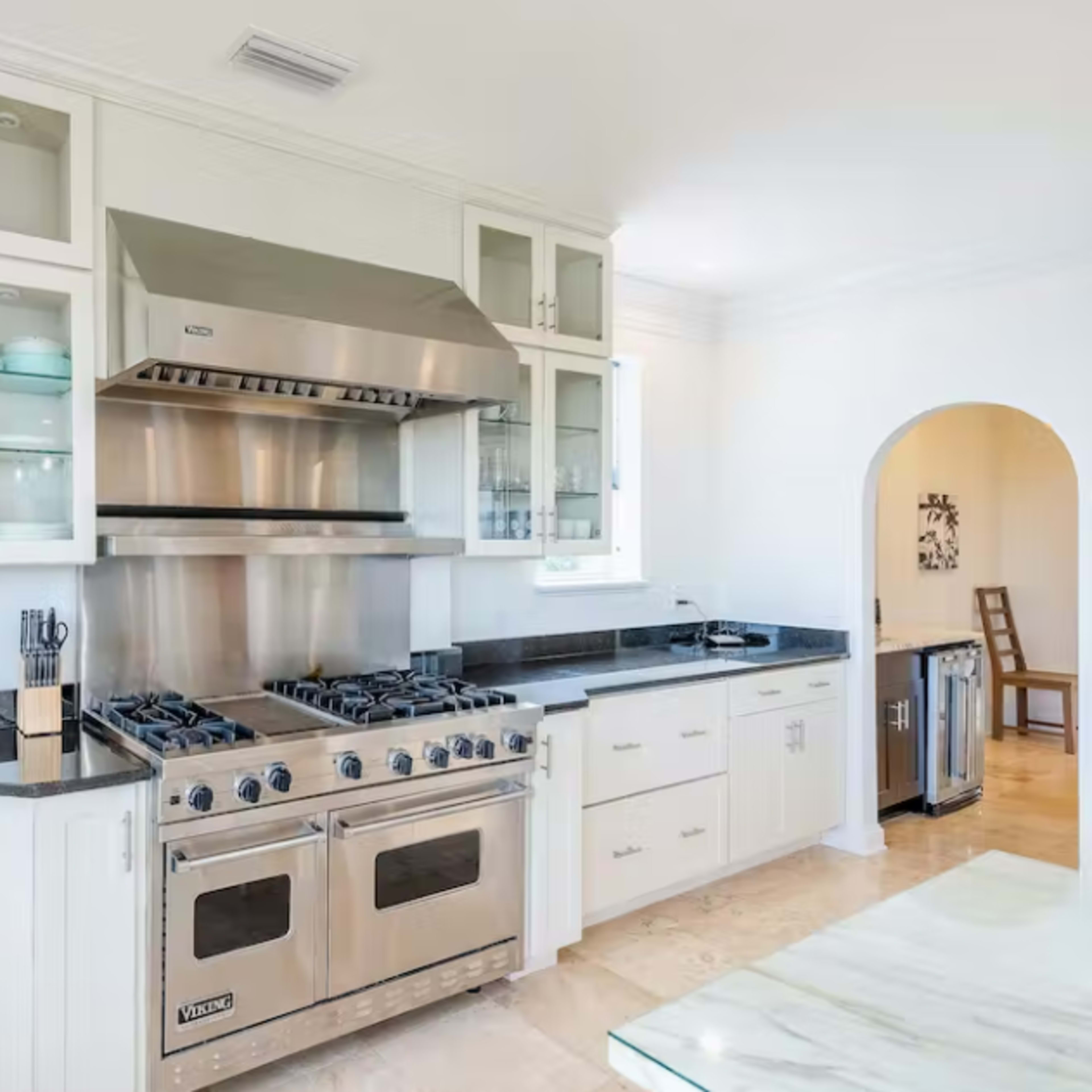 A modern kitchen featuring stainless steel appliances, glass-front cabinets, and a central cooking range with a ventilation hood.
