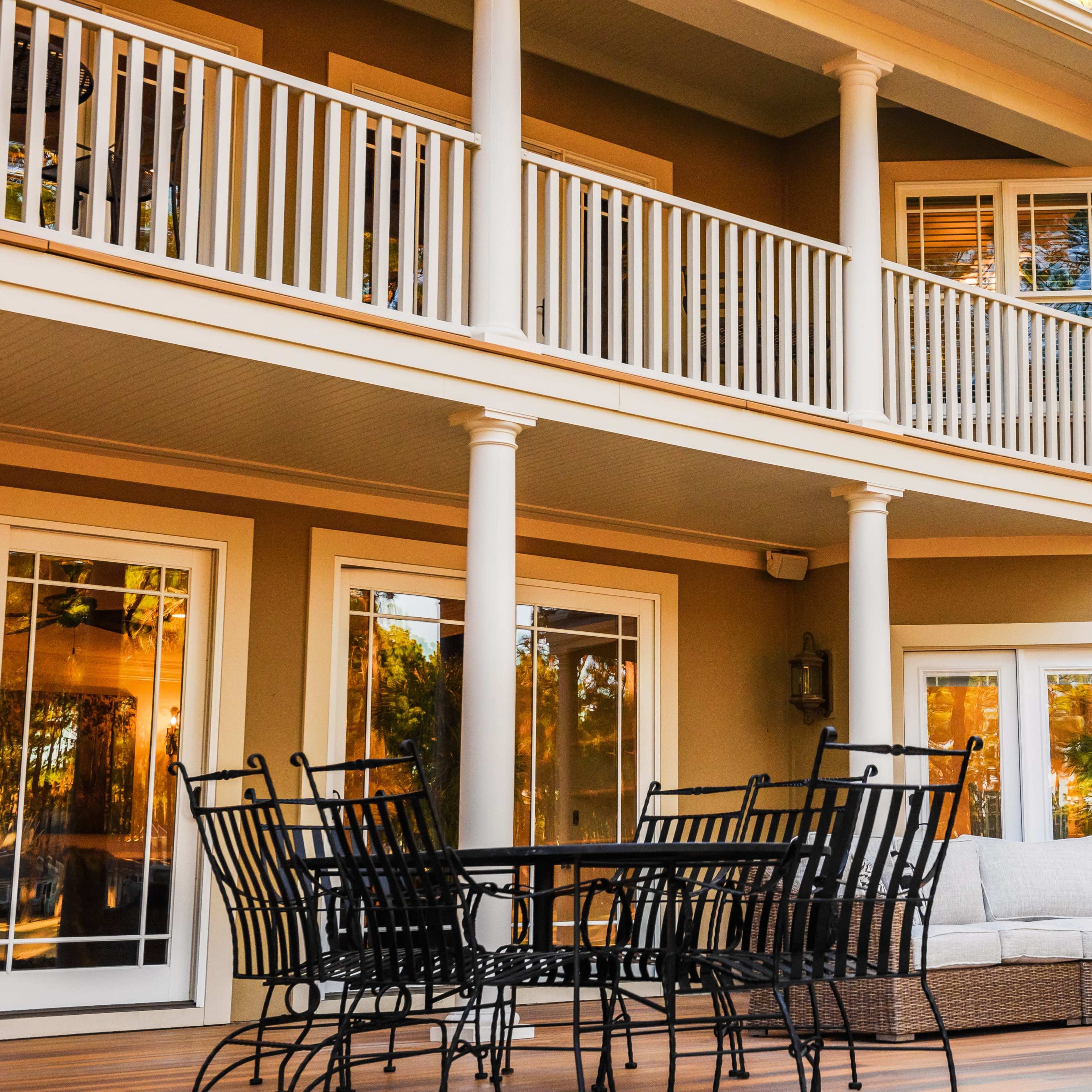 A patio area with a table and chairs, as well as a sofa, beneath a two-story balcony with multiple windows.