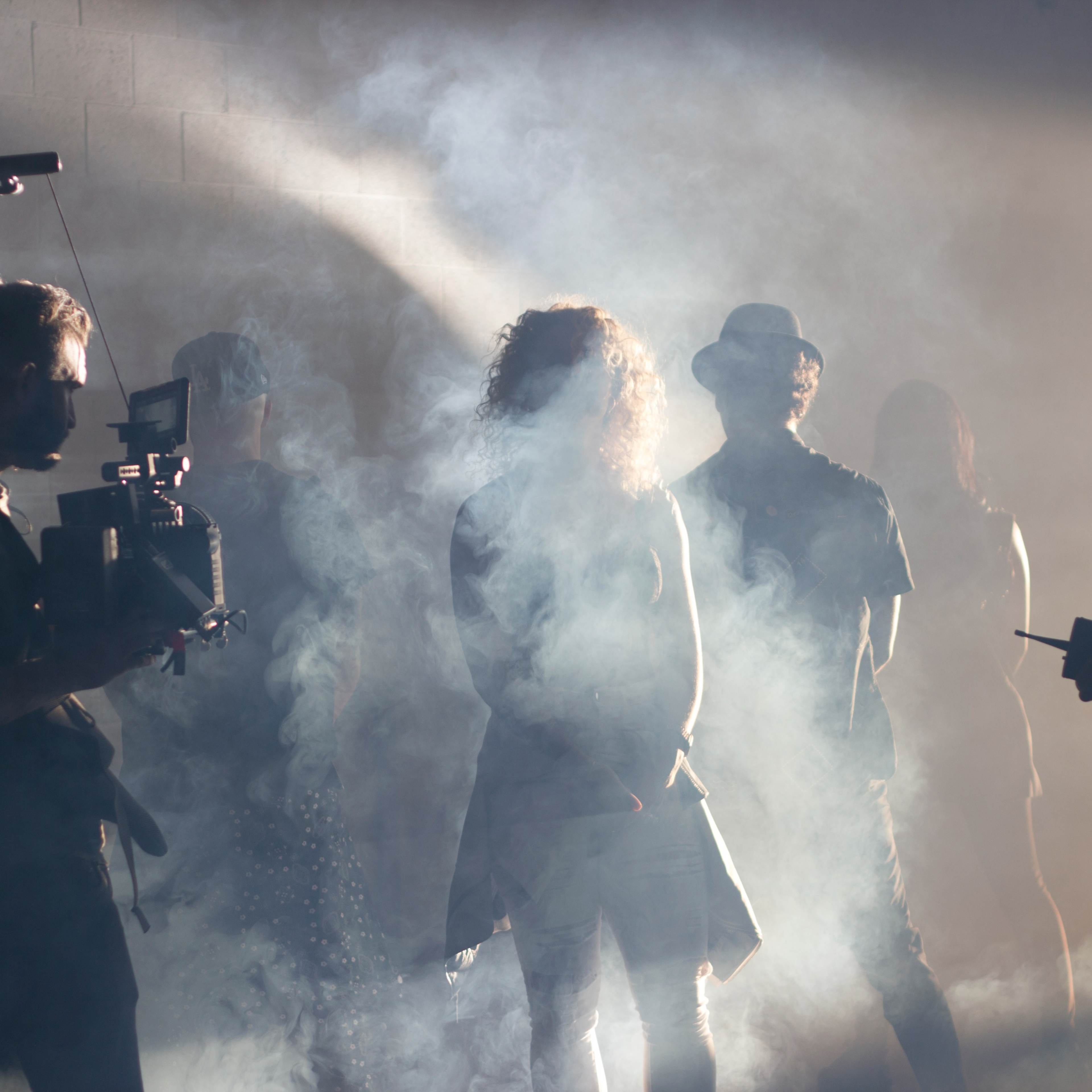 A group of individuals stands in a foggy setting while a person with a camera stabilizer films a scene.