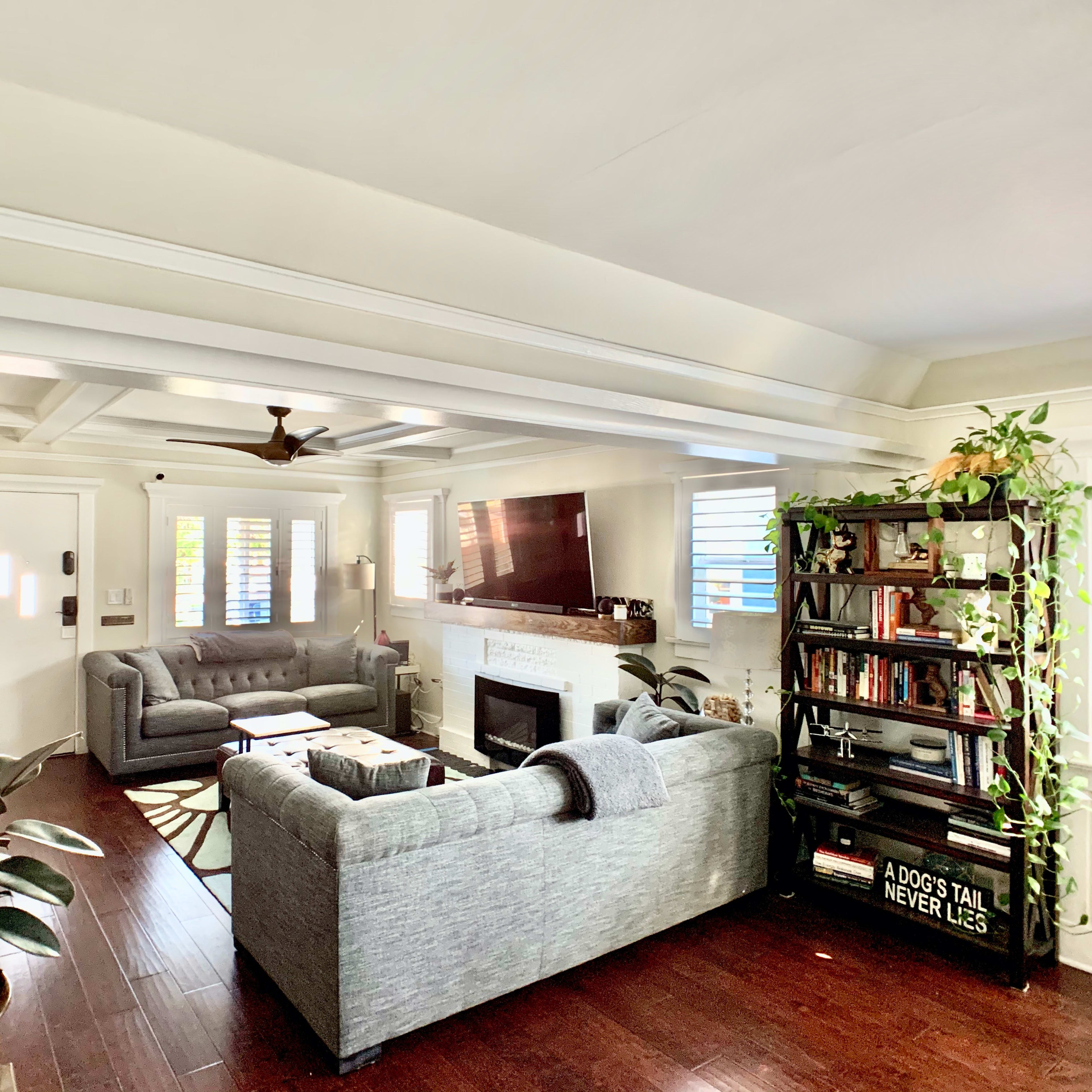 A living room with gray sofas, a coffee table, and a bookshelf, featuring natural light and wooden flooring.