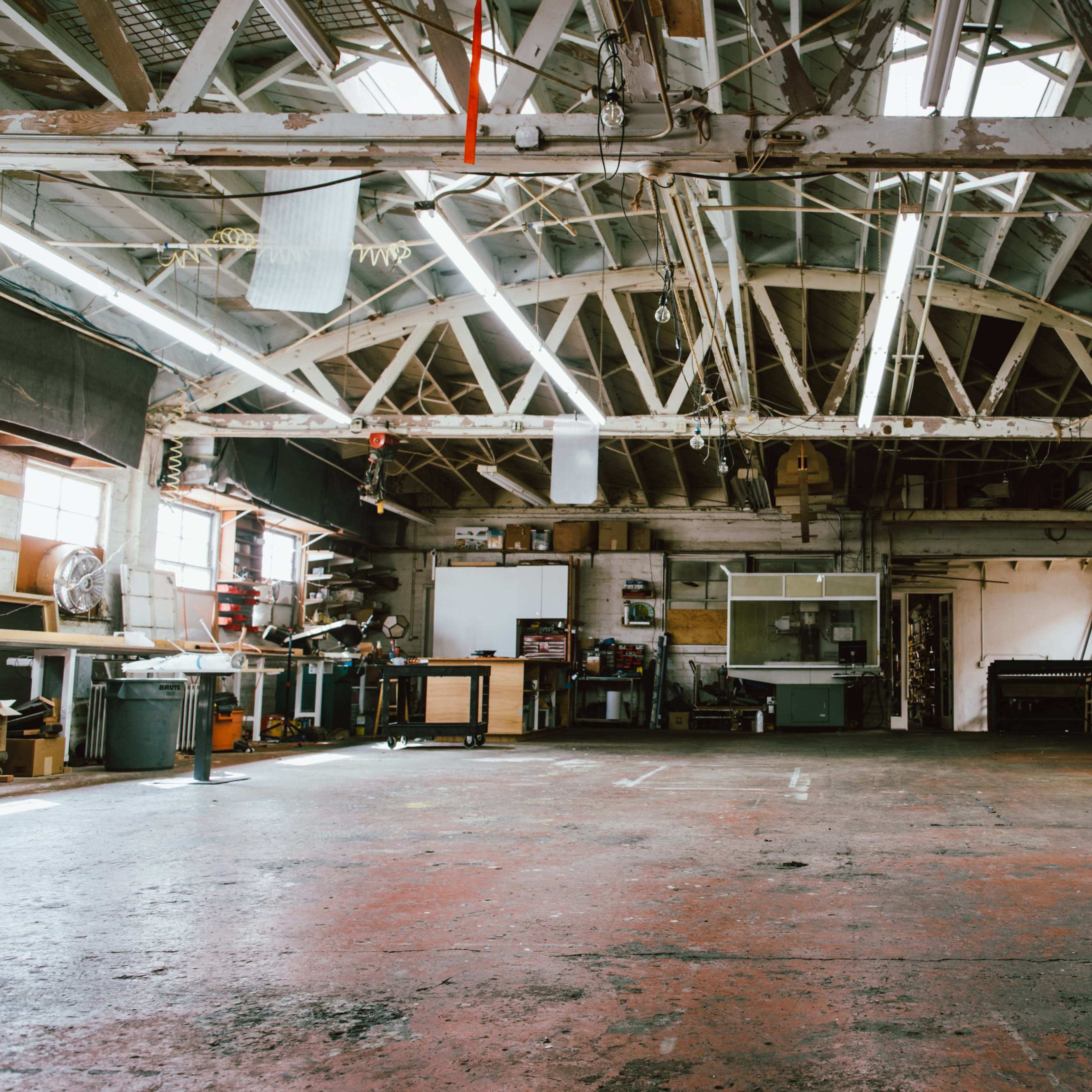 A spacious workshop with high ceilings, exposed beams, and various tools and equipment arranged along the walls.