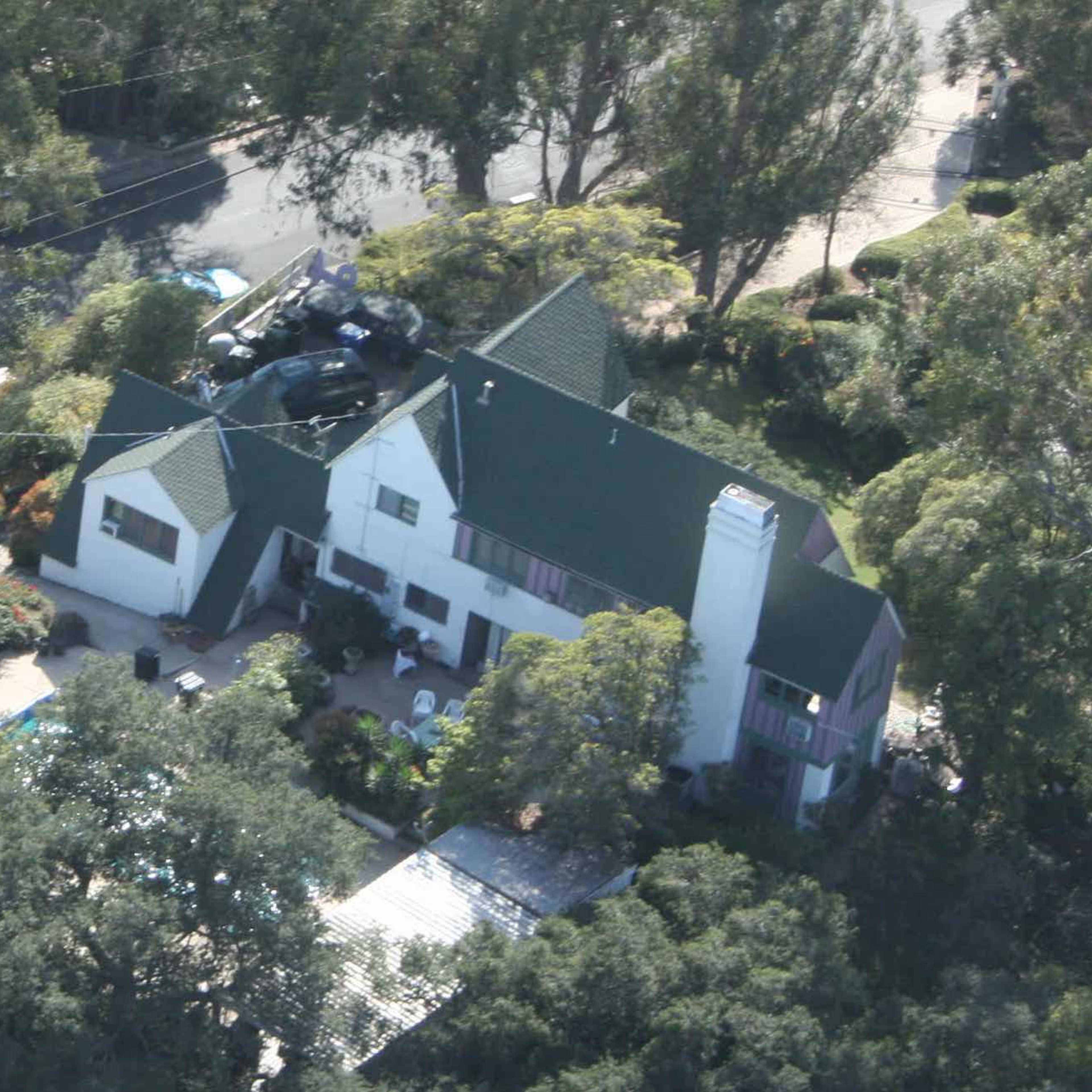 An aerial view of a large house with a green roof surrounded by trees and a neatly landscaped yard.