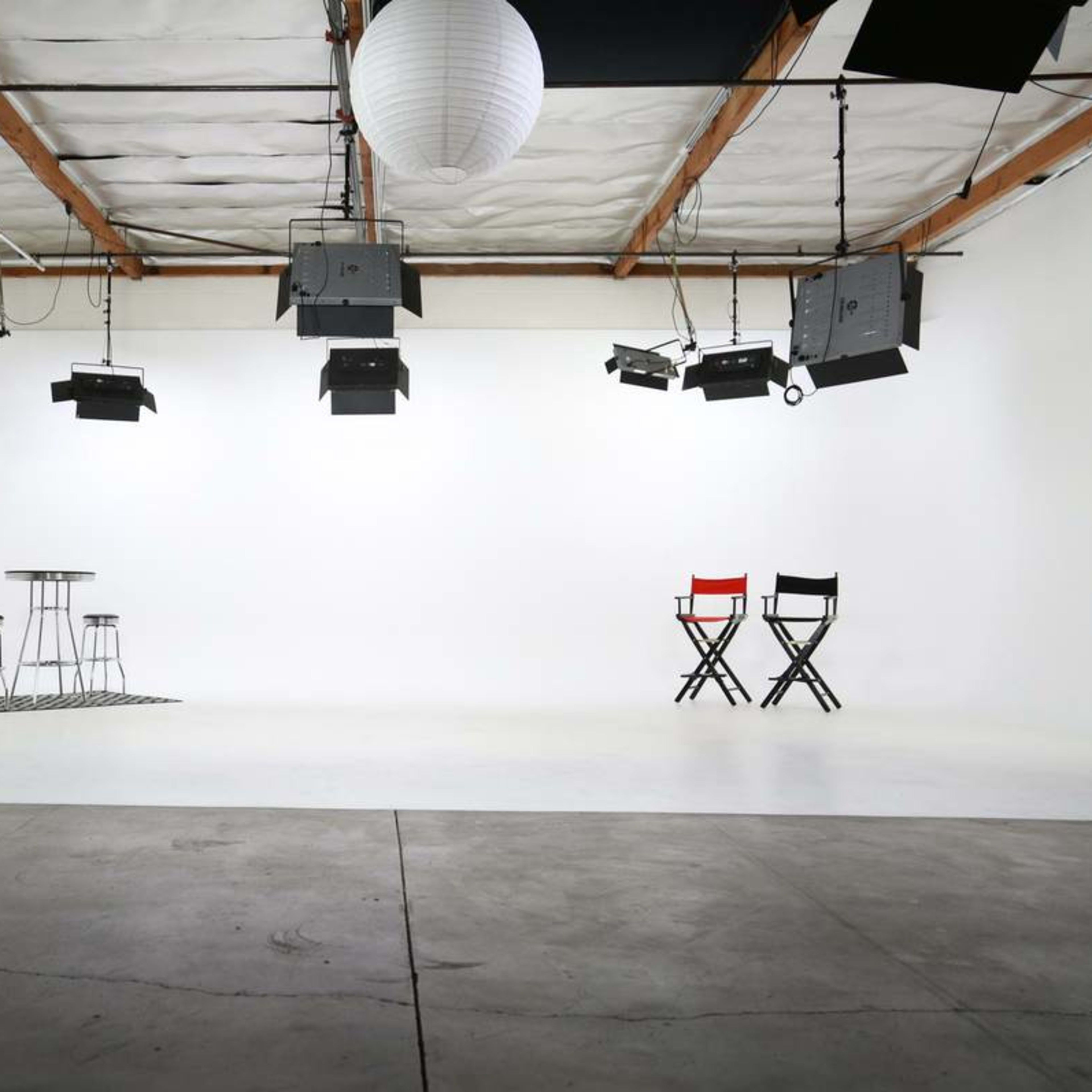 A blank studio space with two chairs, a small table, and multiple overhead lights against a white backdrop.