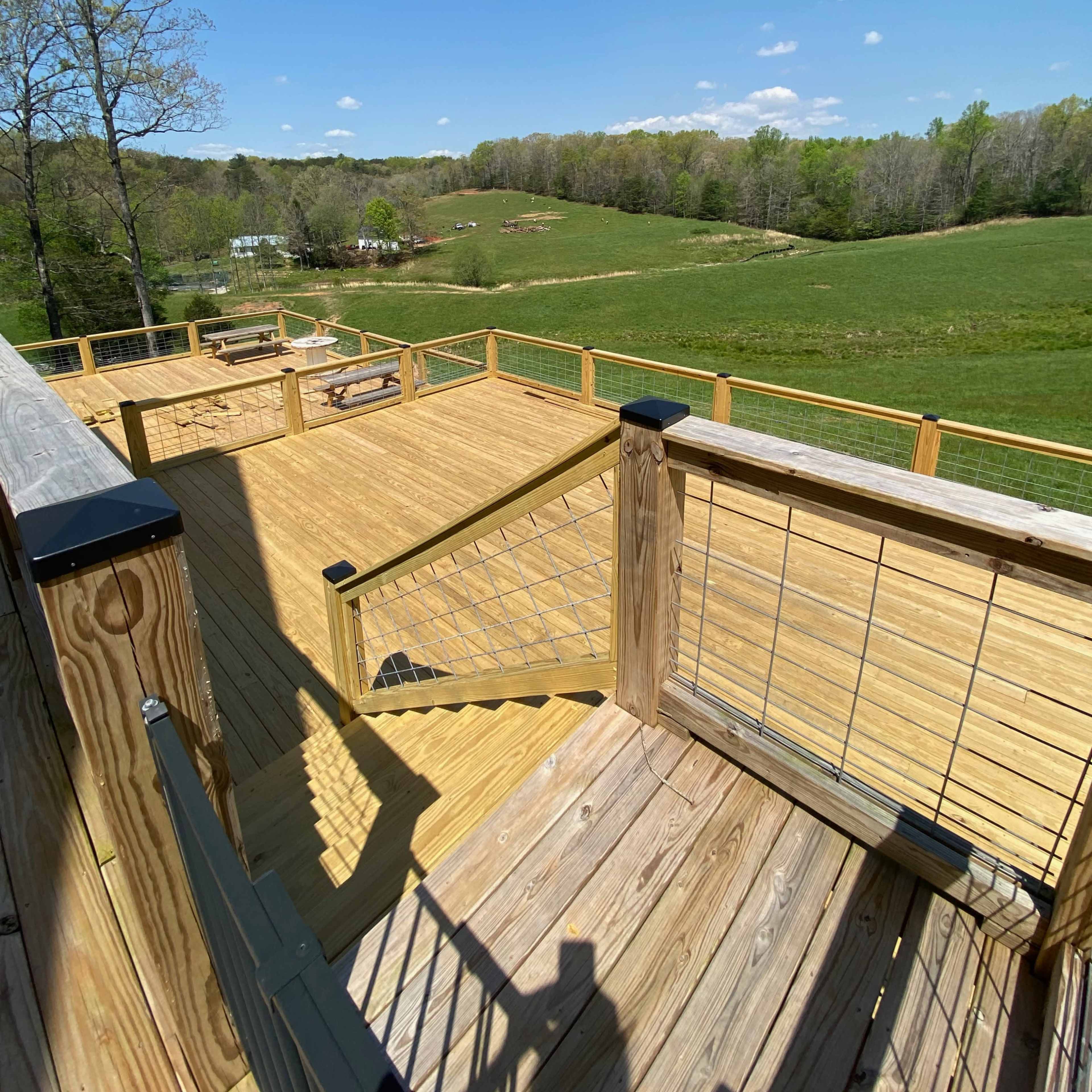 A wooden deck overlooks a green hillside under a clear blue sky.