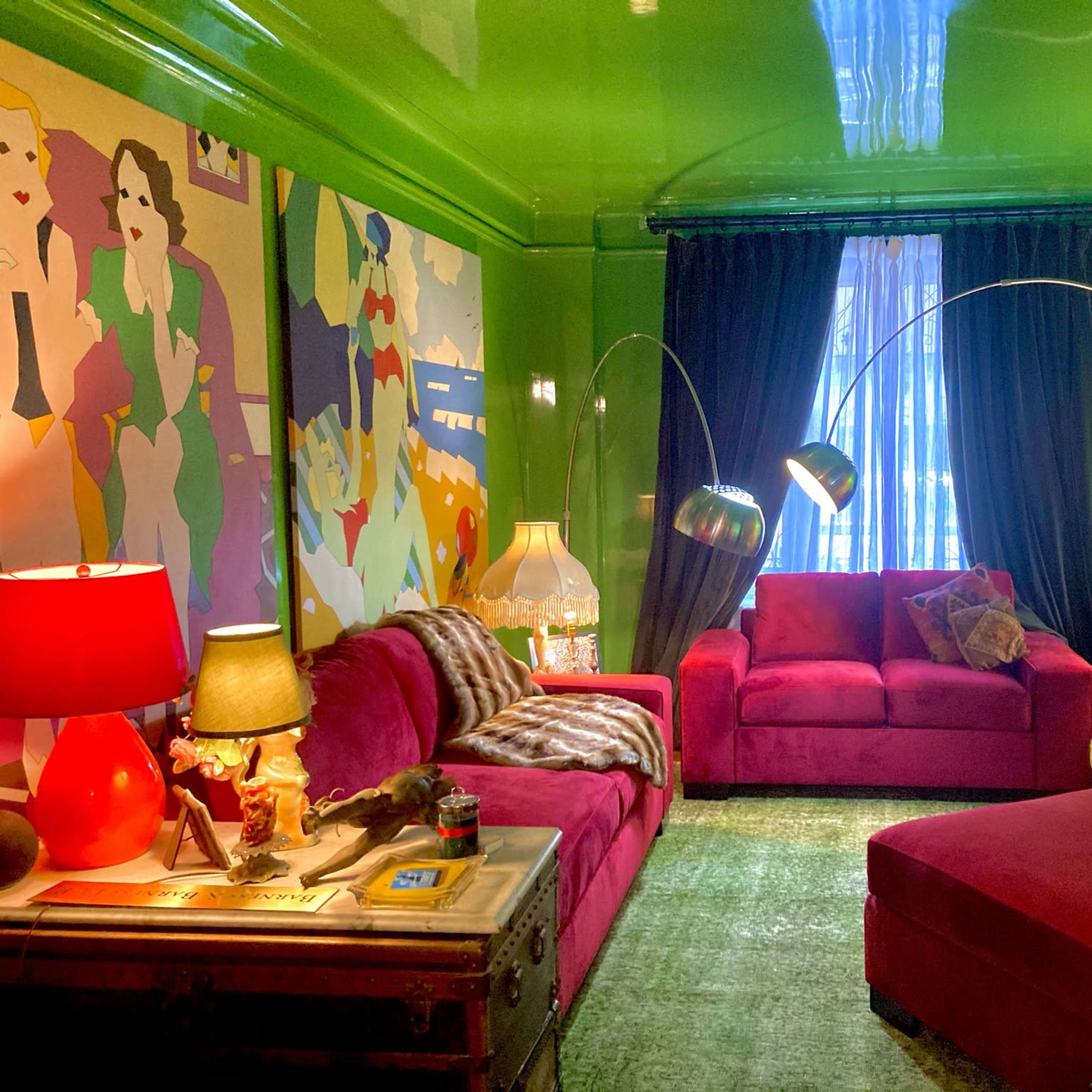 A vibrant living room with green walls, red sofas, colorful artwork, and various light fixtures.