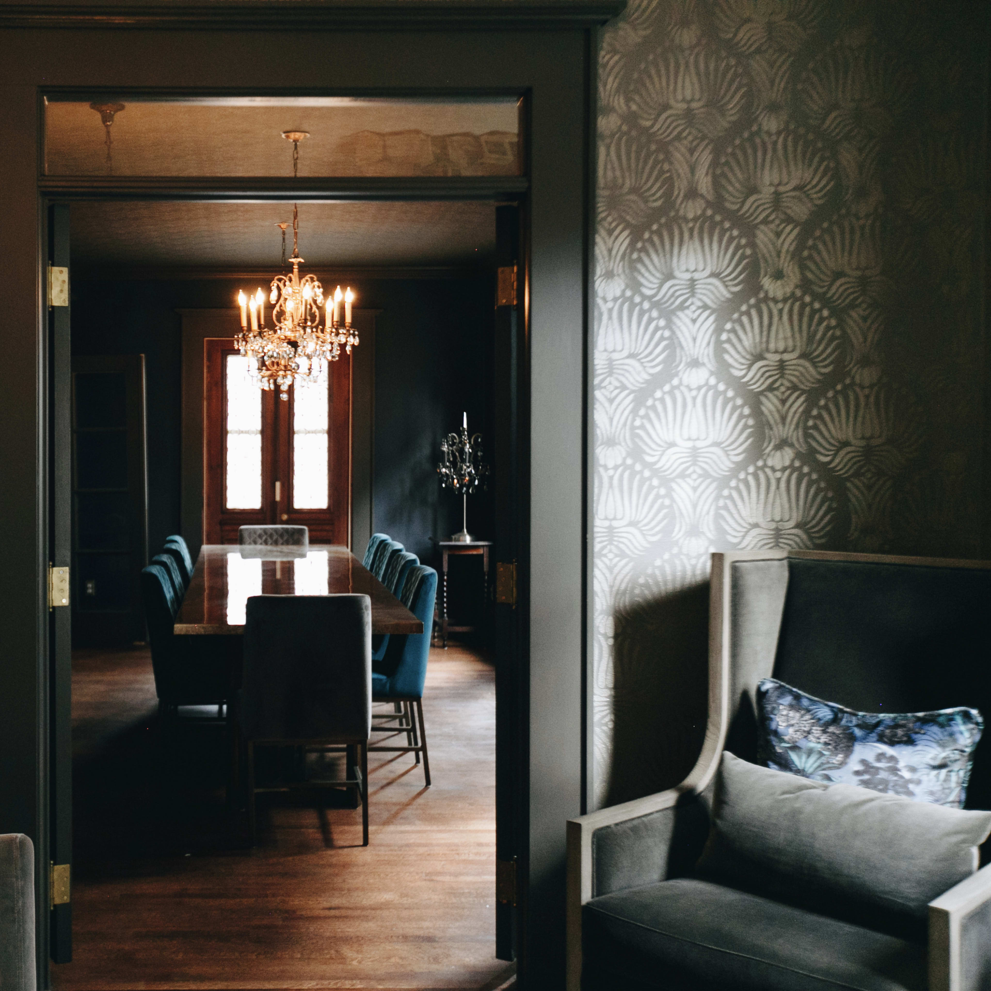 A dining room with a long table and chairs is visible through an open doorway, featuring a chandelier overhead and floral decorations.