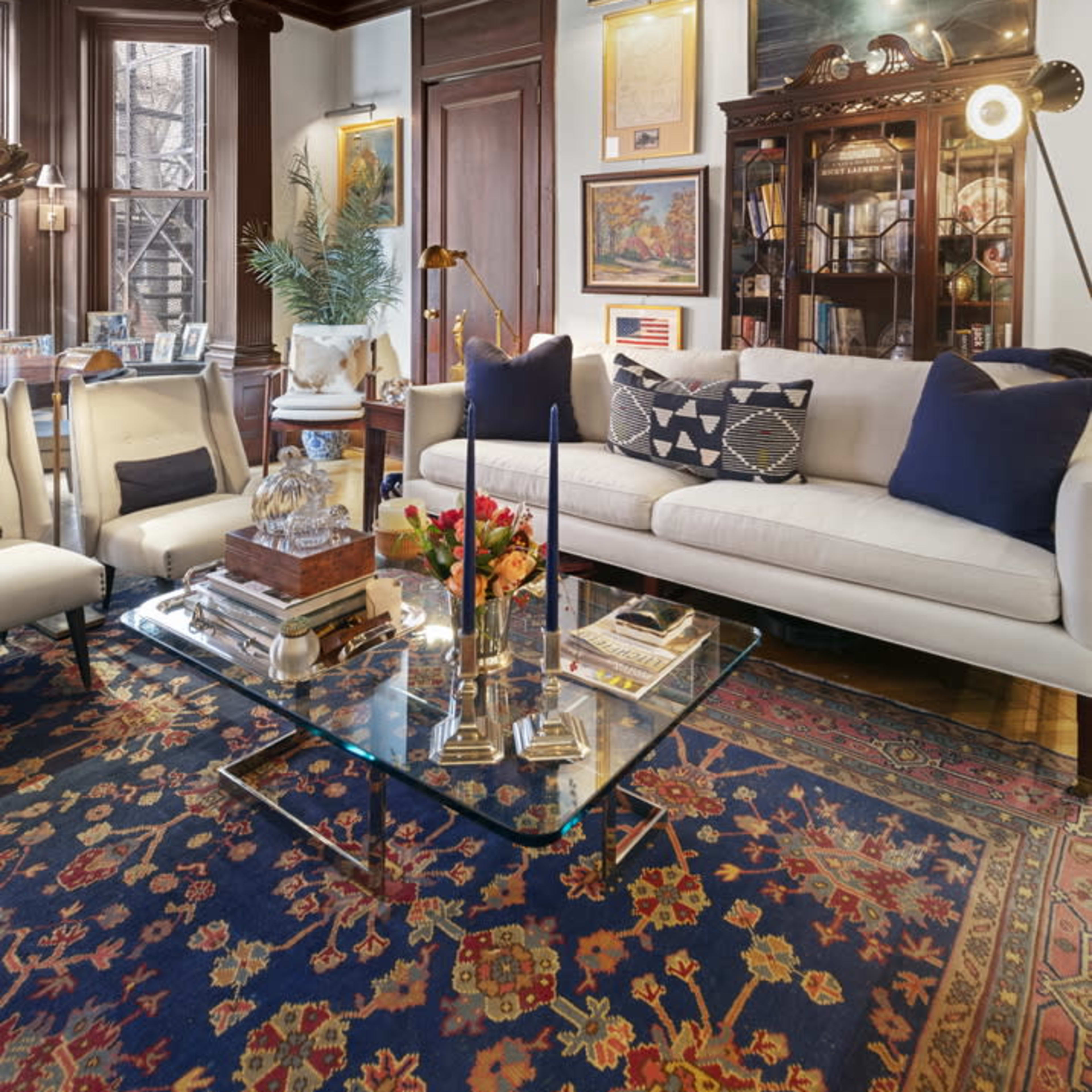 A well-furnished living room with a coffered ceiling, a beige sofa, a glass coffee table, and a vintage-style shelving unit filled with books and decorative items.