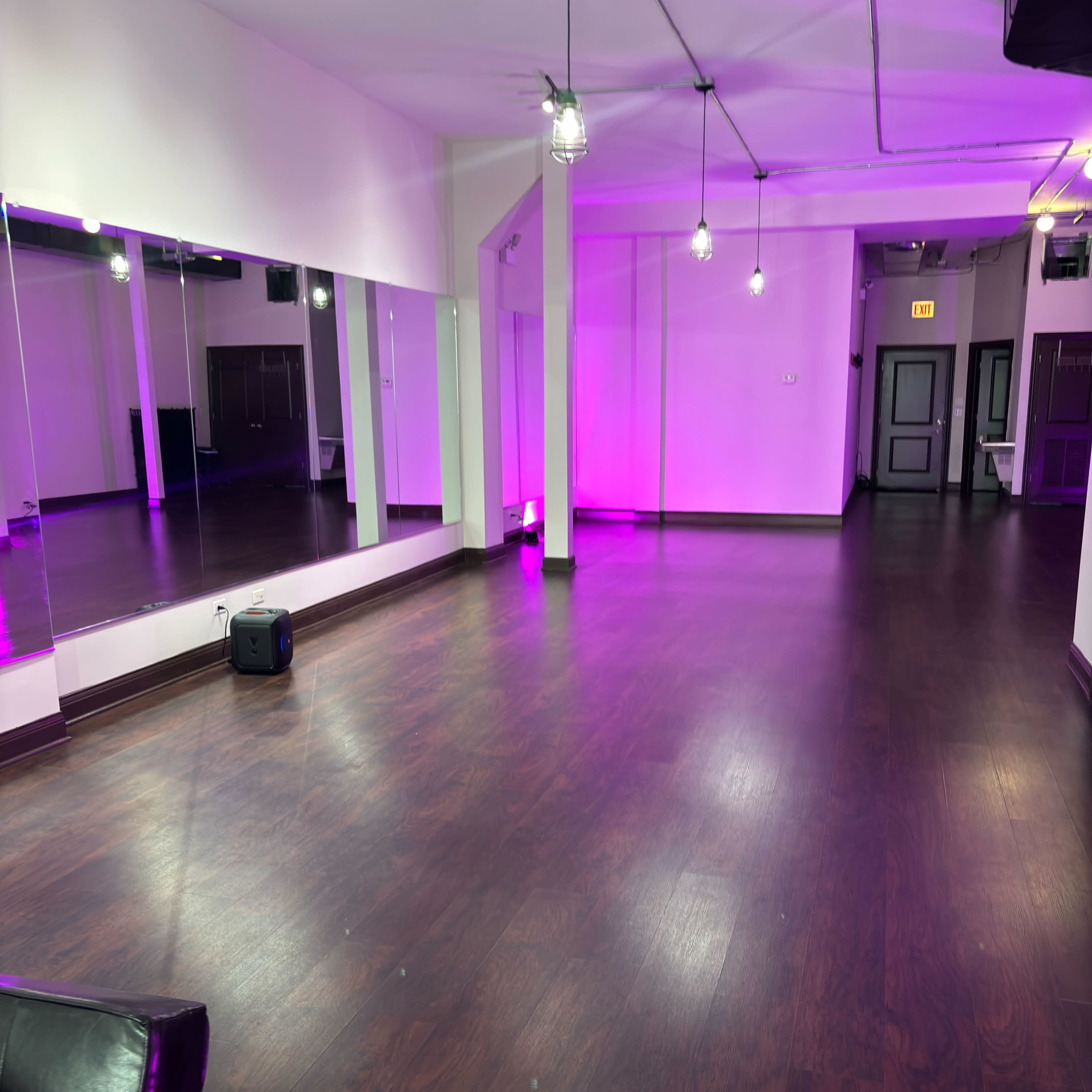 A spacious, well-lit dance studio with mirrors on one wall and purple lighting accents.