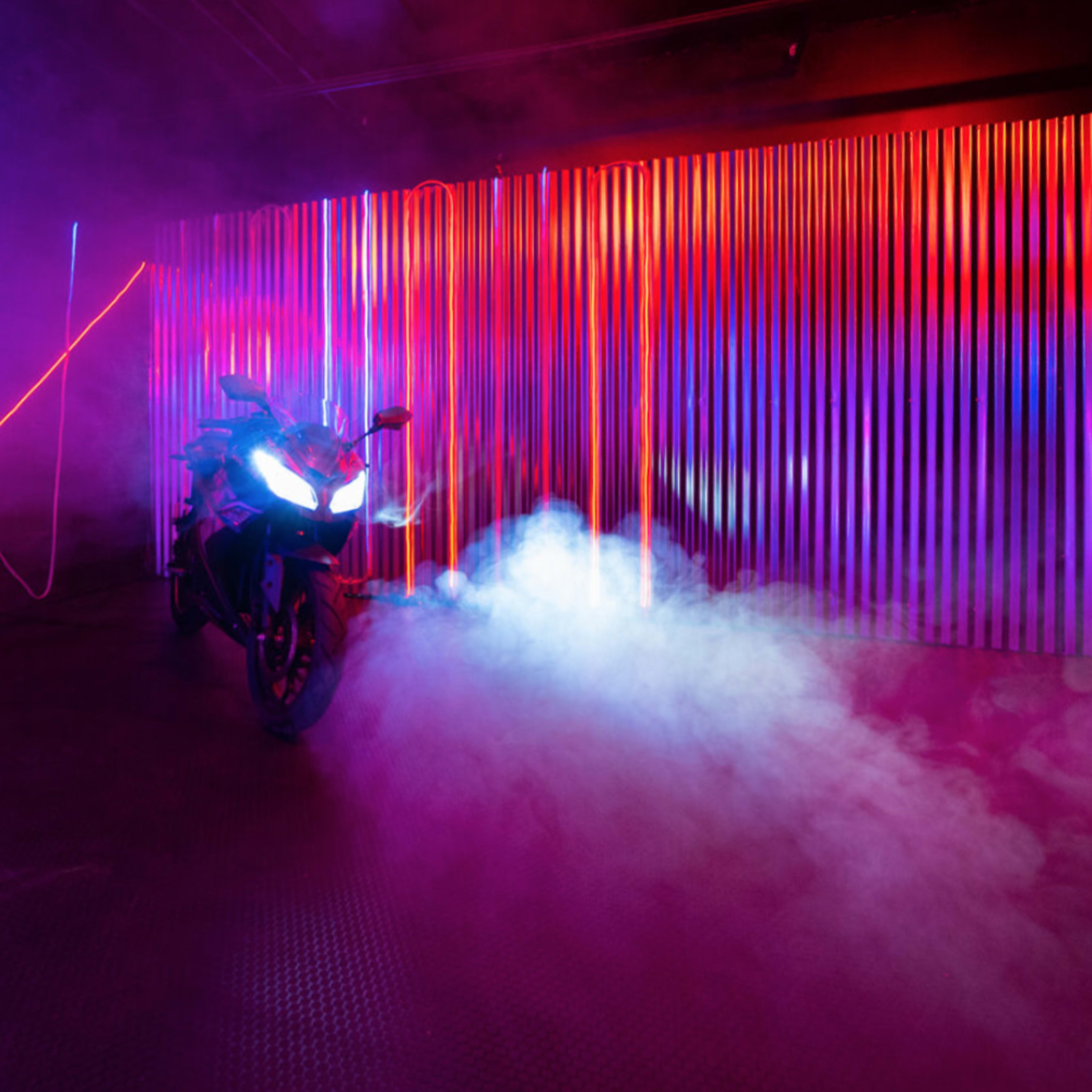 A motorcycle is parked in a dimly lit space with colorful neon lights and smoke effects.