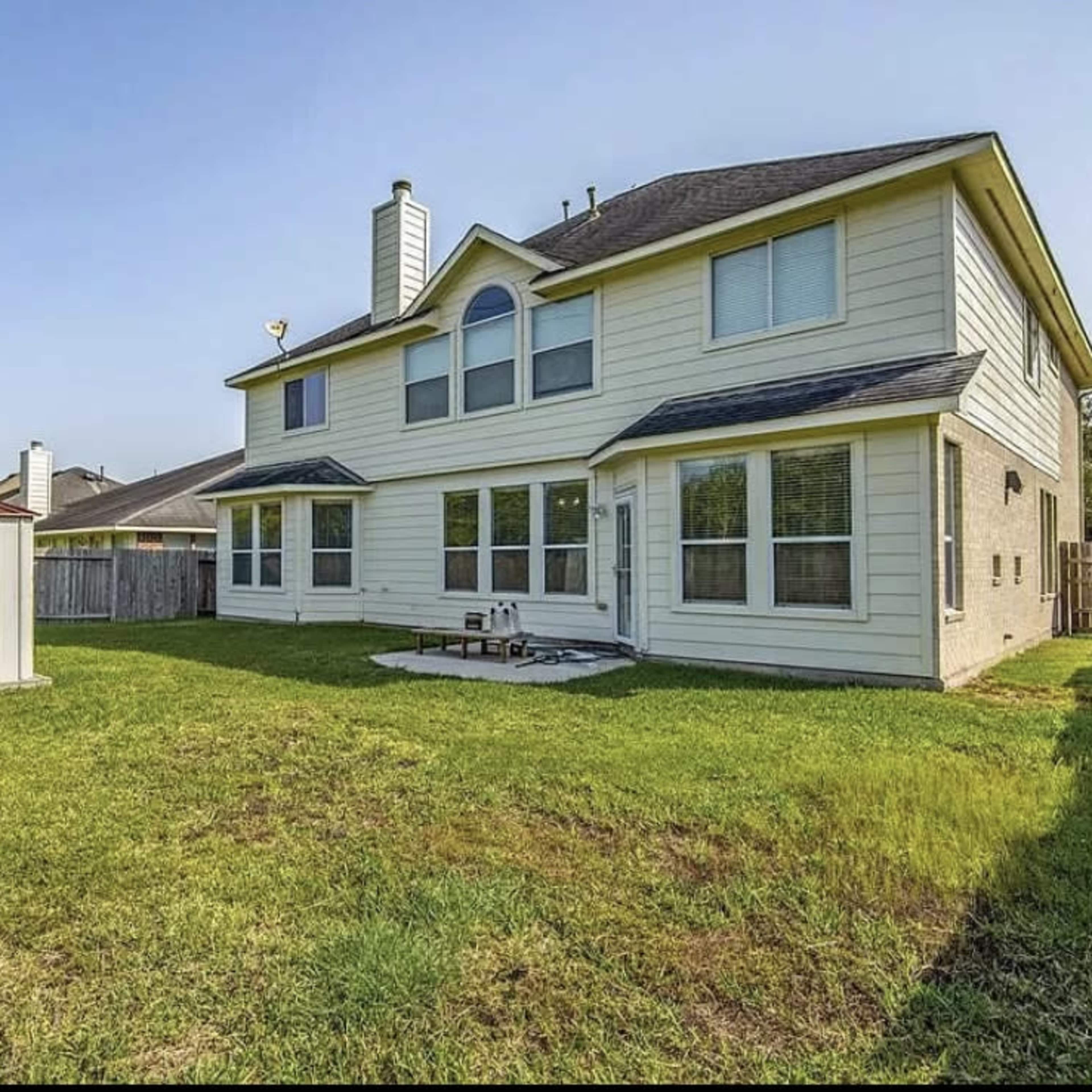 A two-story house with a fenced backyard, a small storage shed, and a patio area on the grass.