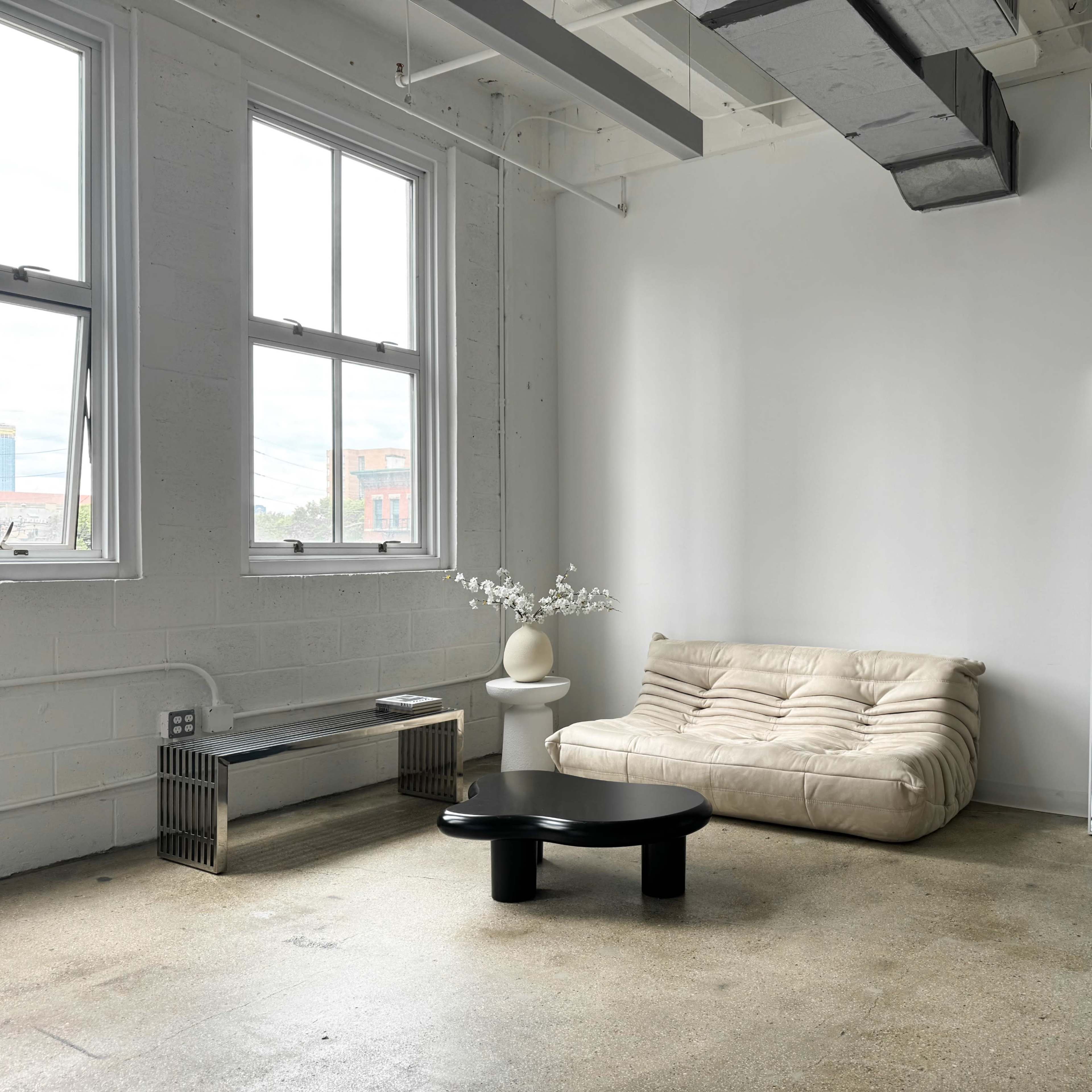 A minimalist room featuring a white couch, a black coffee table, a large mirror, and a plant on a side table.
