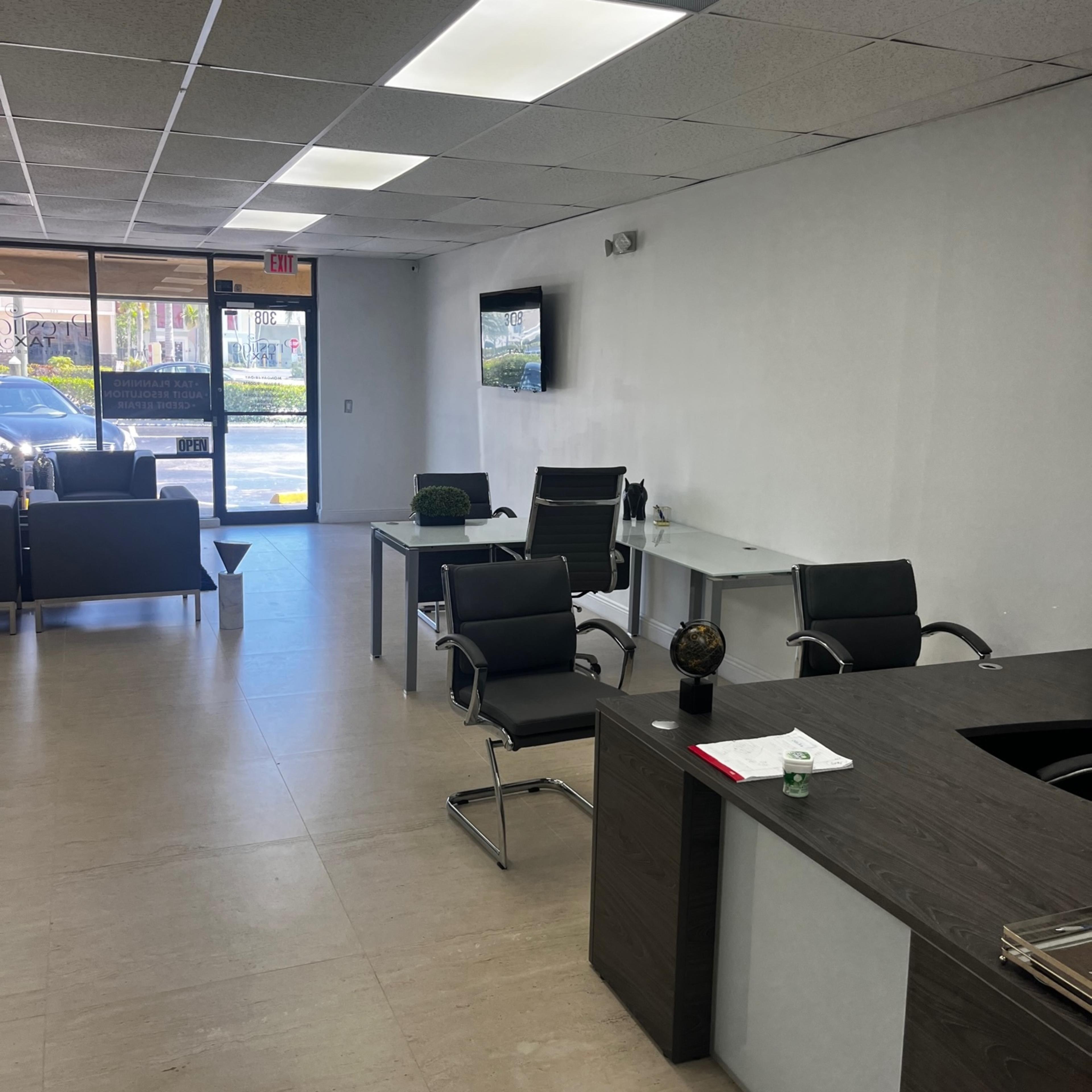 An office interior with a reception area featuring a desk, several chairs, and a television mounted on the wall.