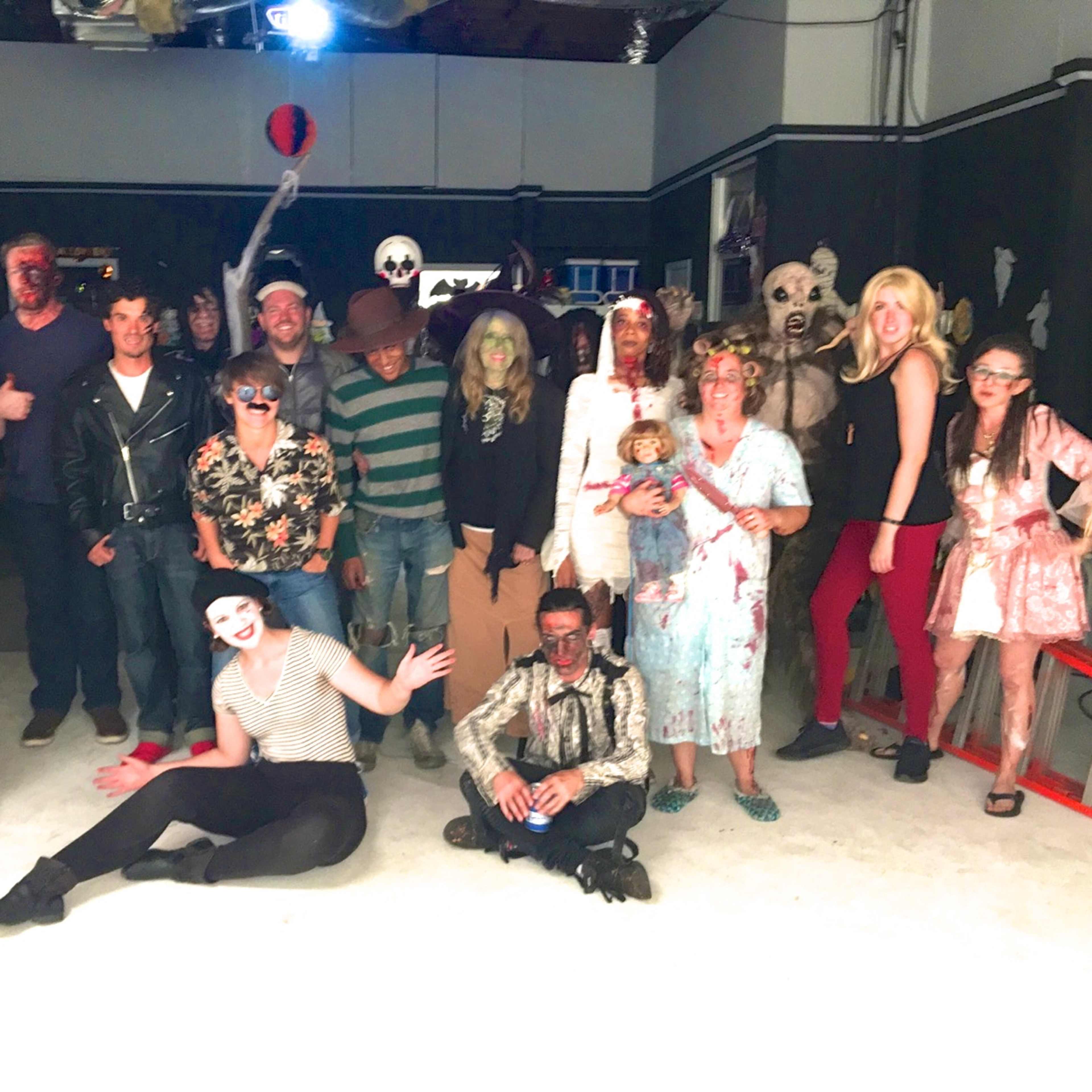 A group of people in costume poses for a photo in a decorated indoor space for a Halloween celebration.