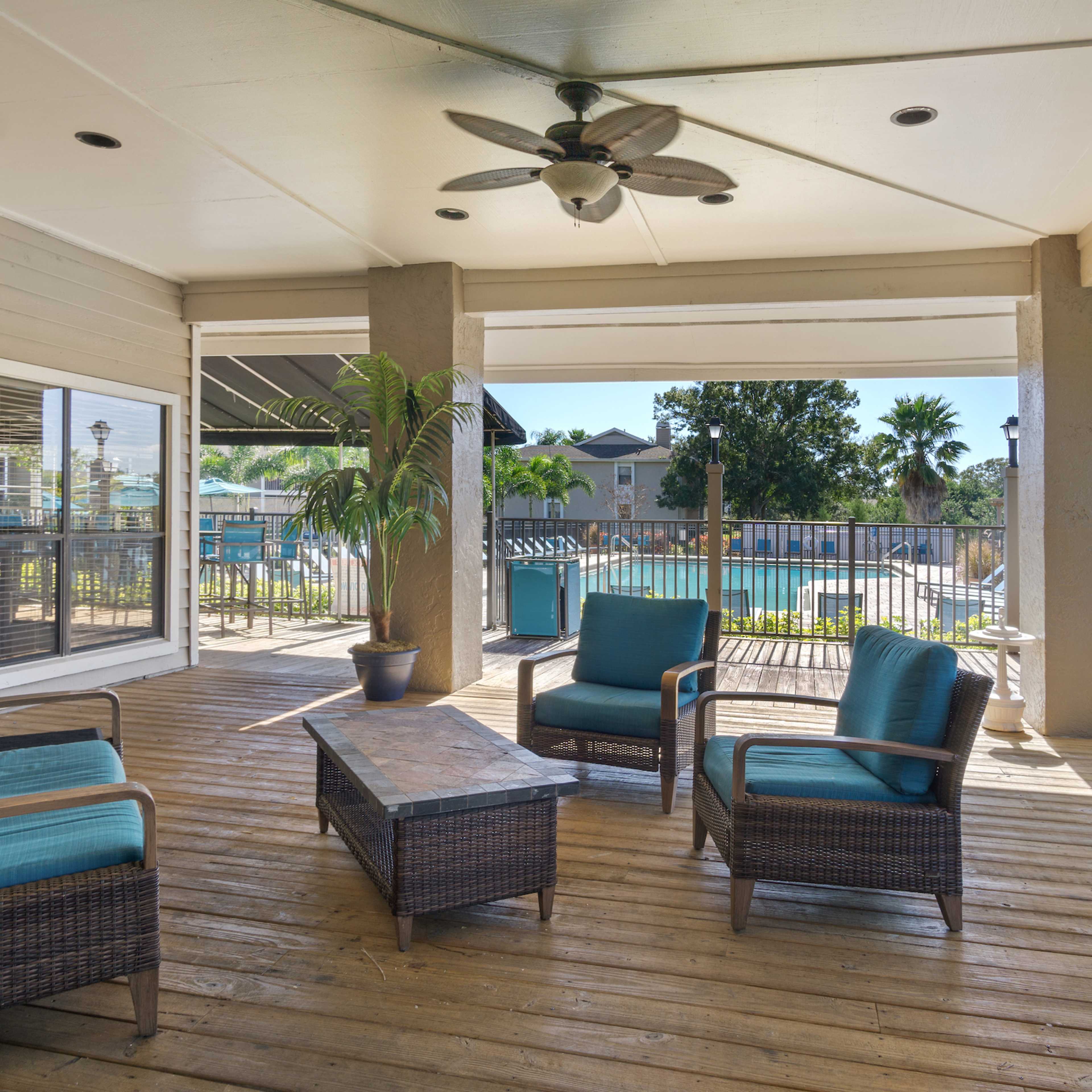A patio area with wicker chairs and a table, overlooking a swimming pool surrounded by palm trees.