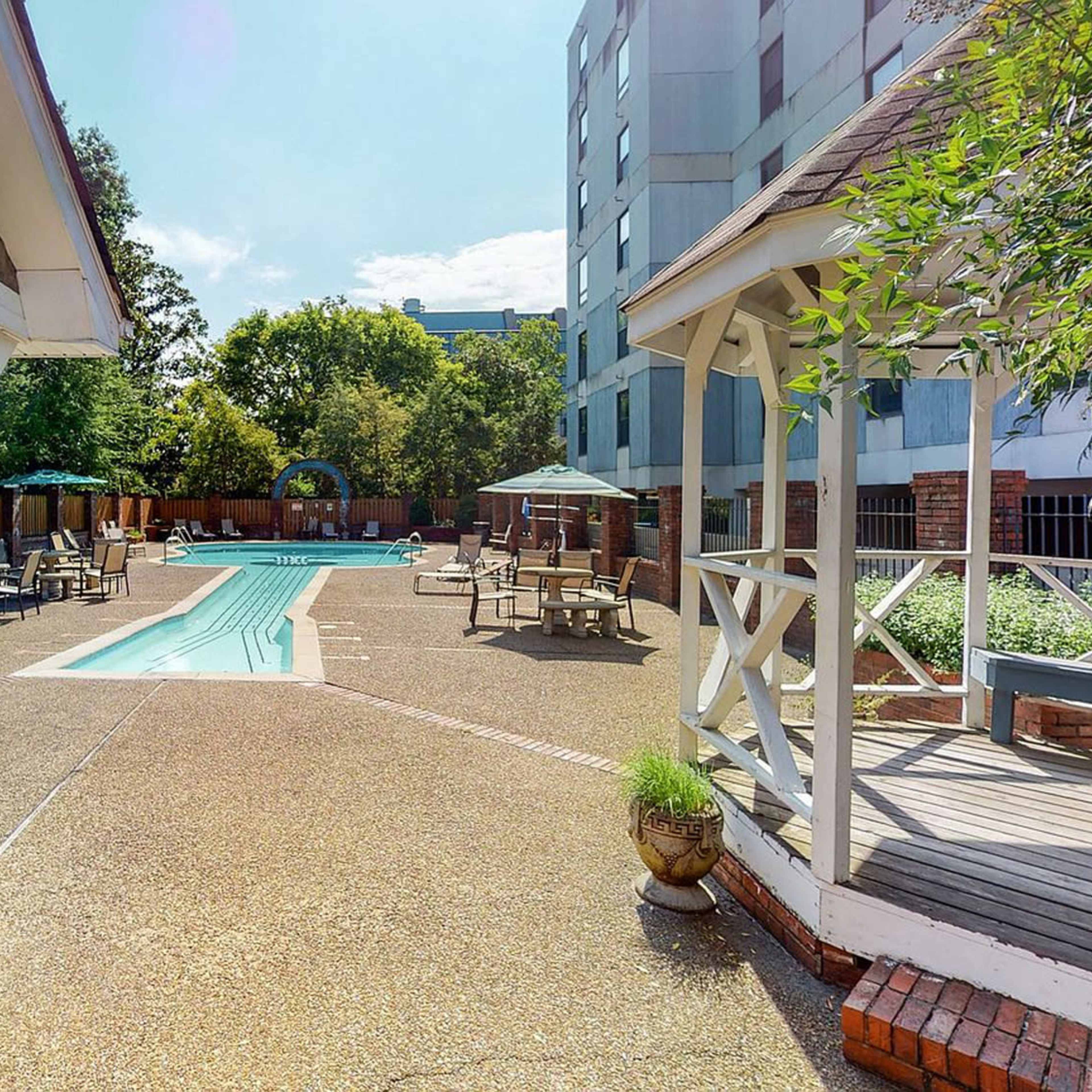 A pool area with lounge chairs and umbrellas, surrounded by buildings and trees.