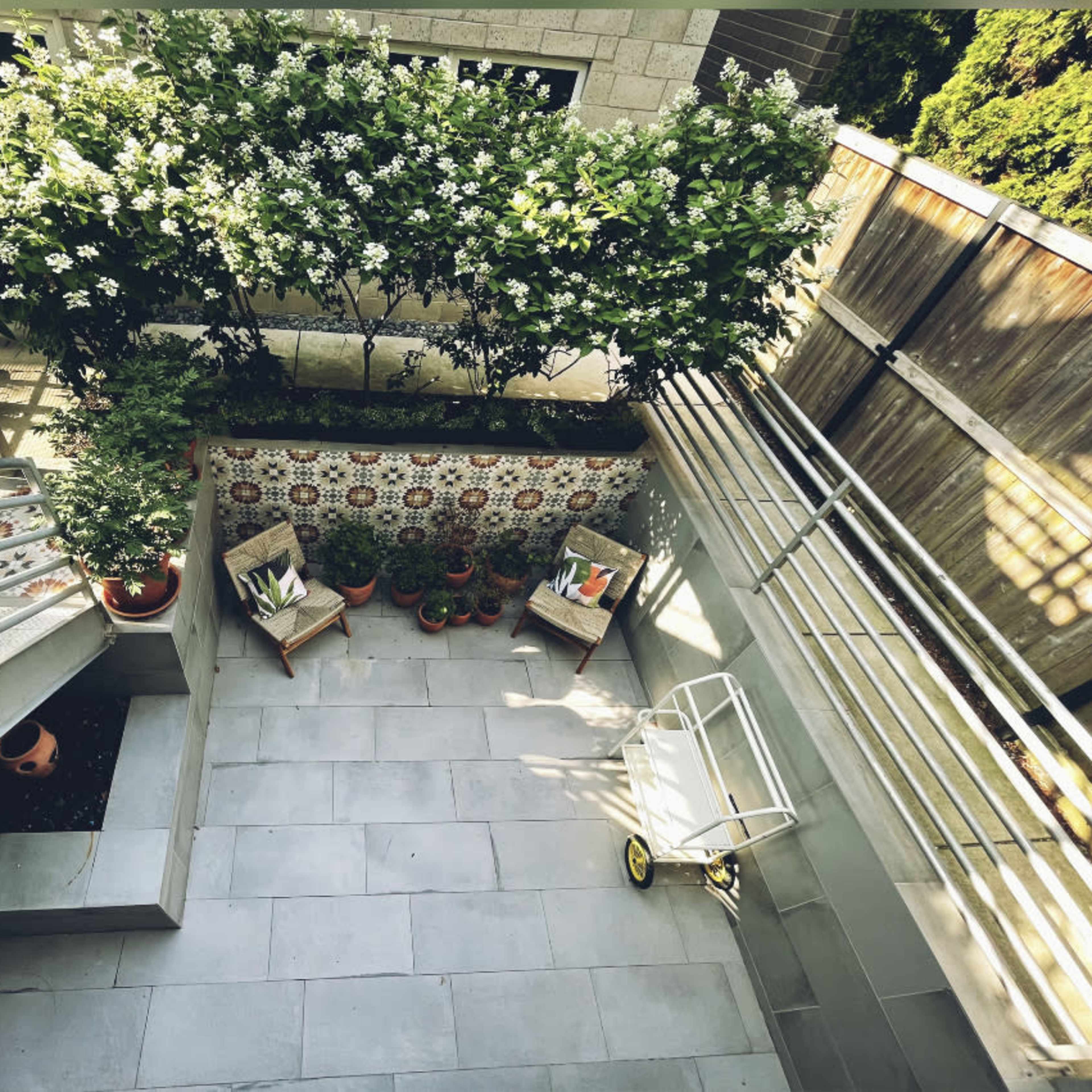 An aerial view of a small courtyard featuring tiled walls, potted plants, two chairs, and a staircase.
