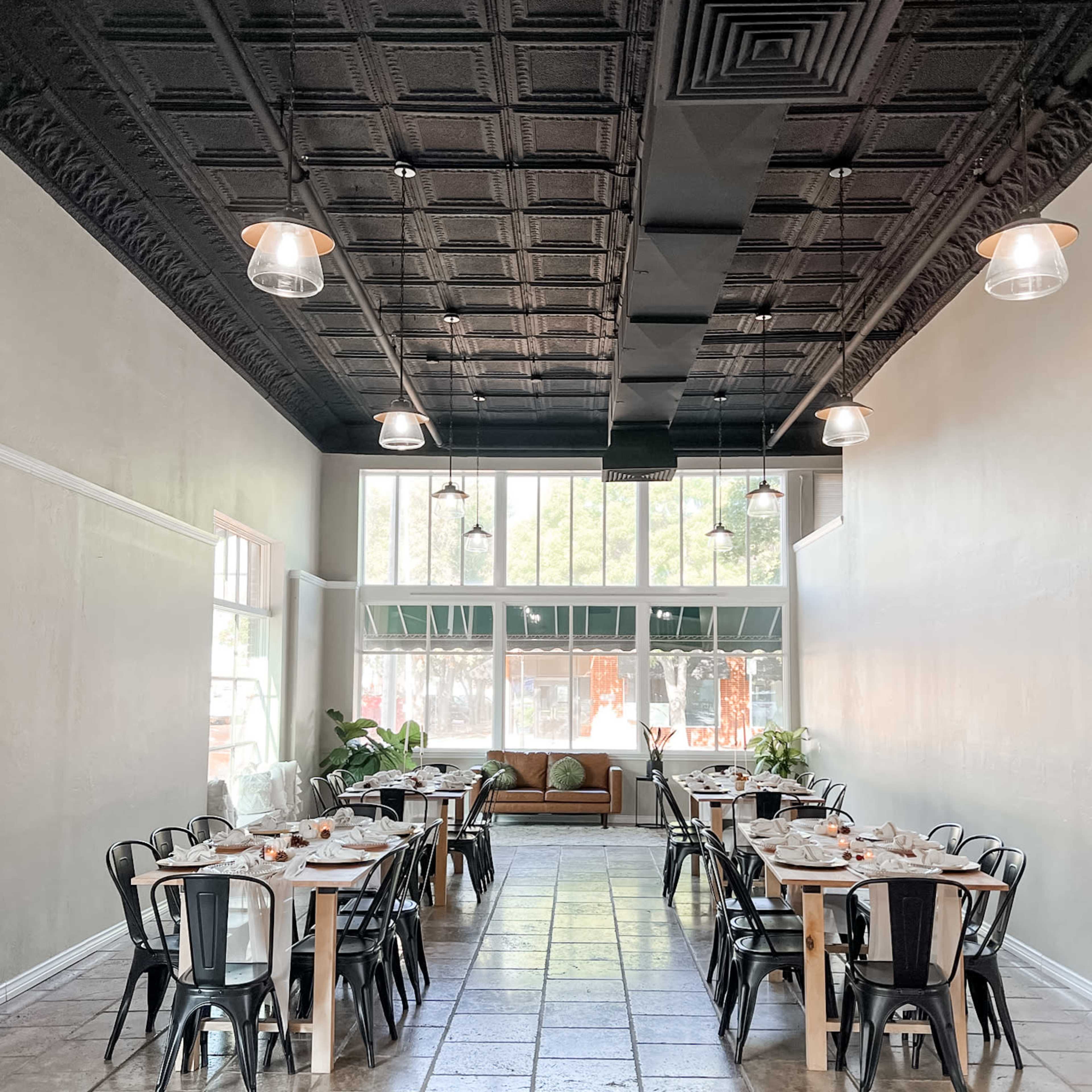 A spacious dining area with tables set for meals, black chairs, and large windows allowing natural light to enter.