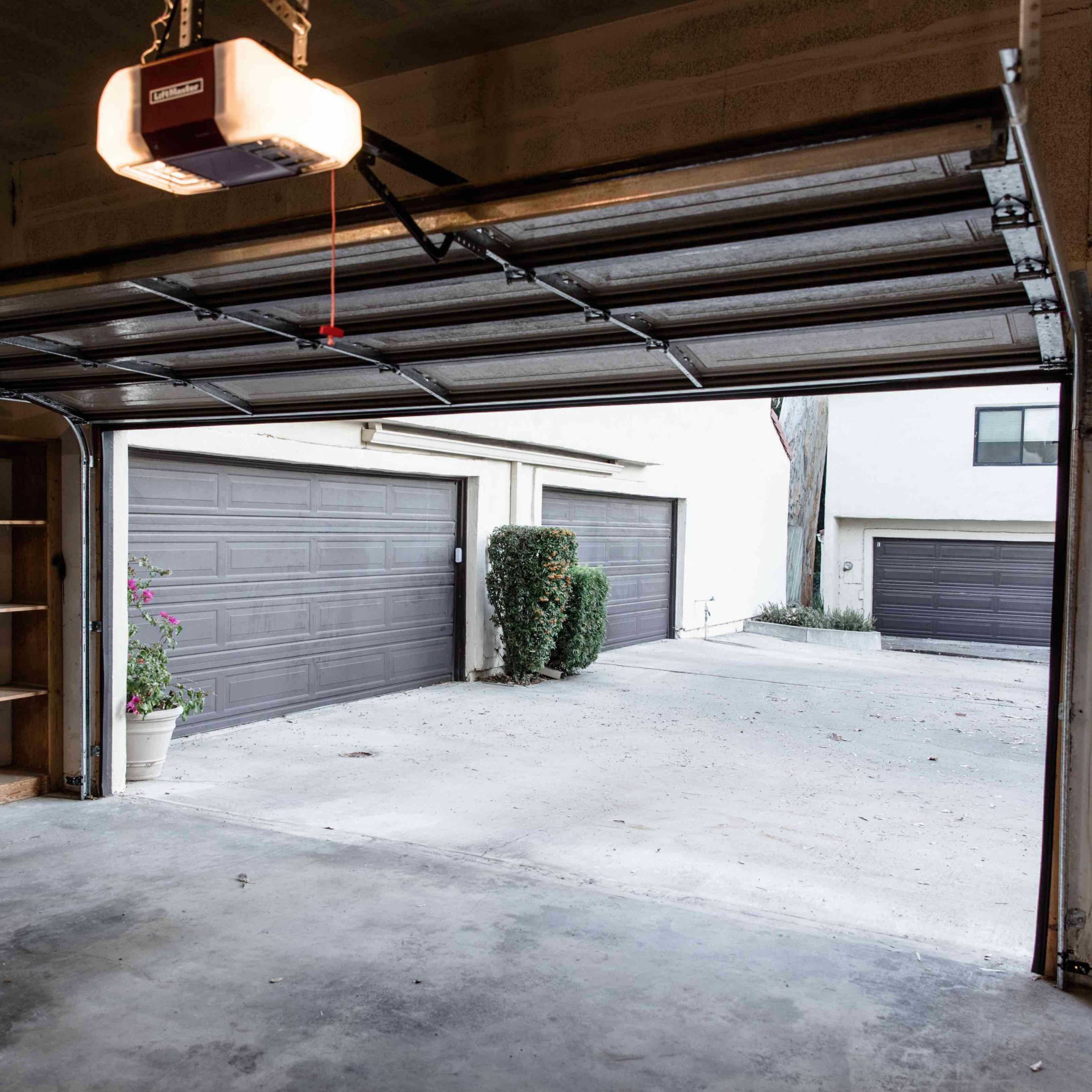 The interior of a garage with an open door, revealing a driveway and several closed garage doors in the background.