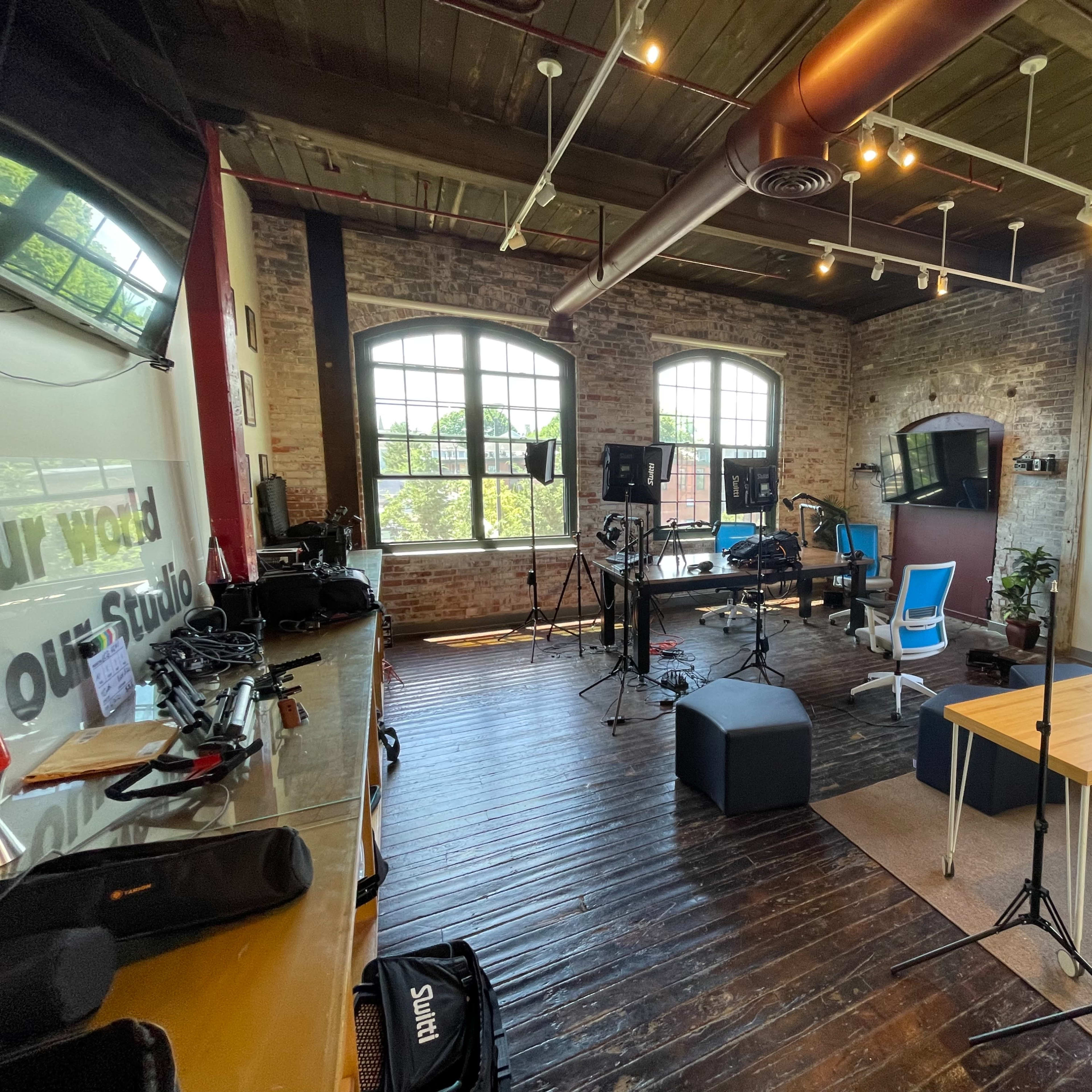 A spacious studio with wooden floors, large windows, and equipment set up for production.