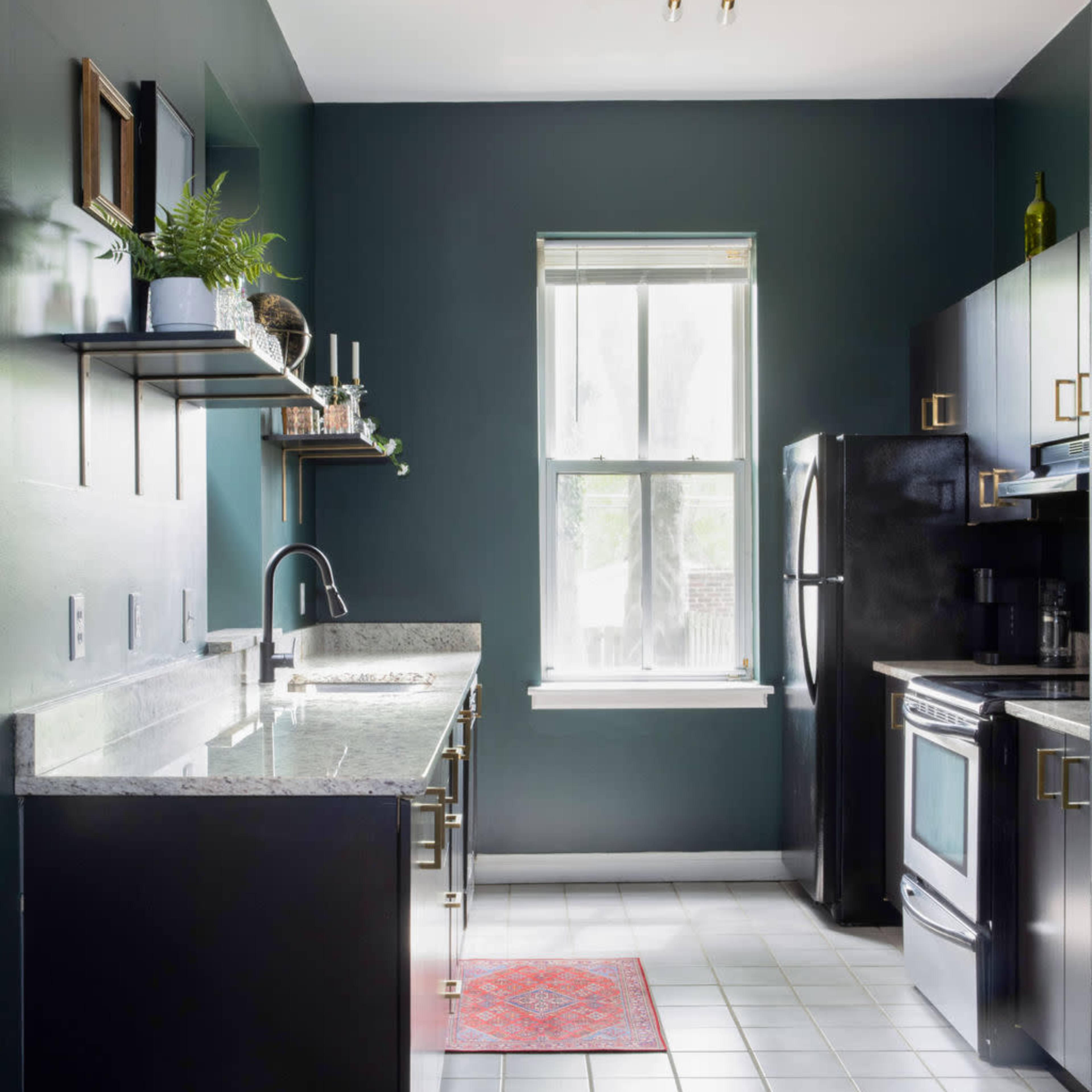 The kitchen features dark green walls, black cabinetry, a marble countertop, and stainless steel appliances with a window allowing natural light.