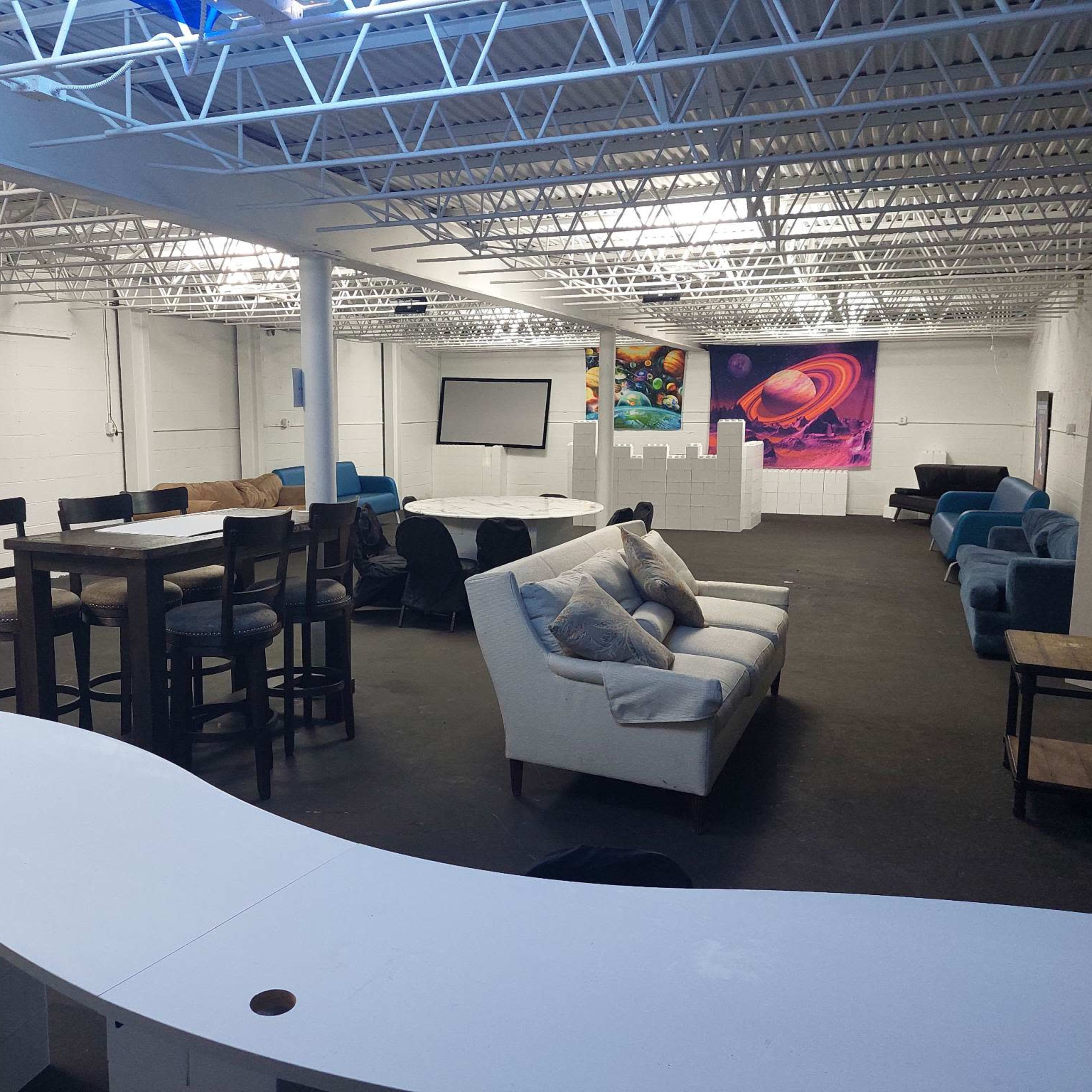 A spacious, well-lit communal area with various seating arrangements, including tables and couches, and a large screen at one end.