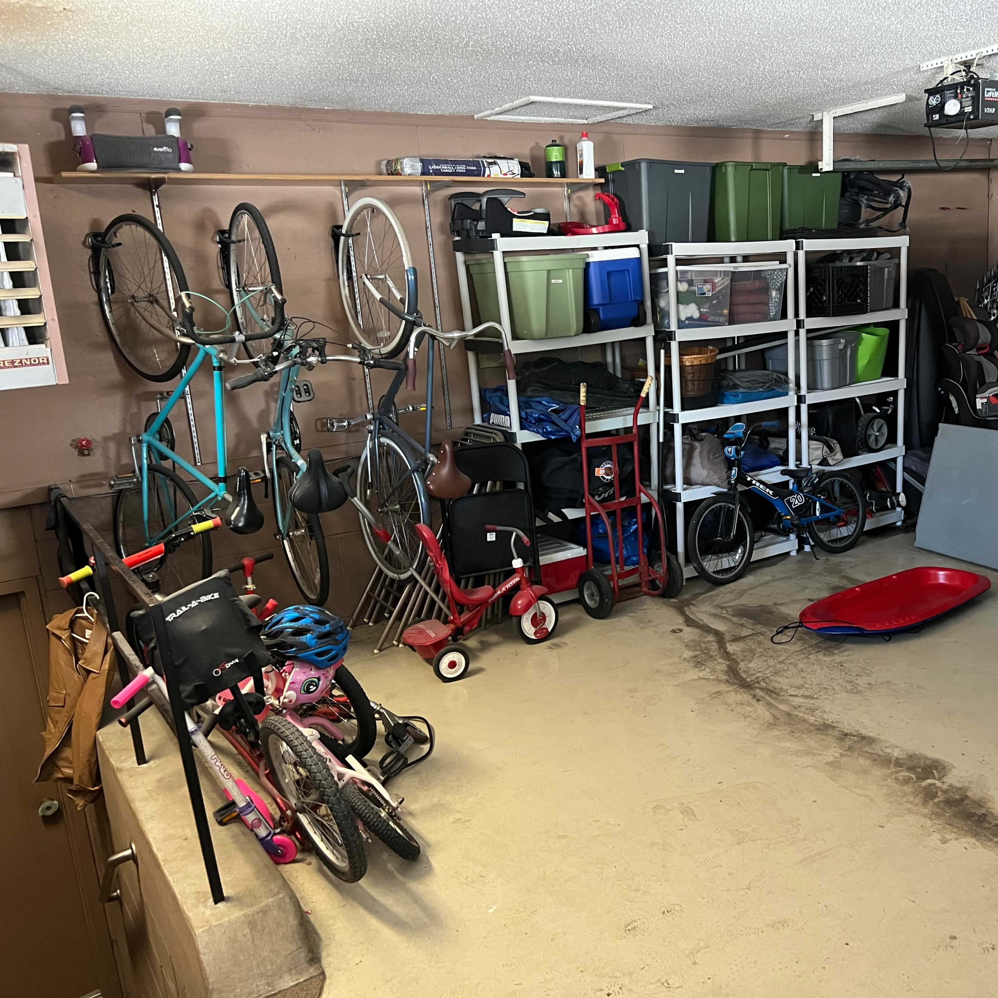 The garage contains bicycles, storage bins, and various items organized on shelving units alongside a parked vehicle.