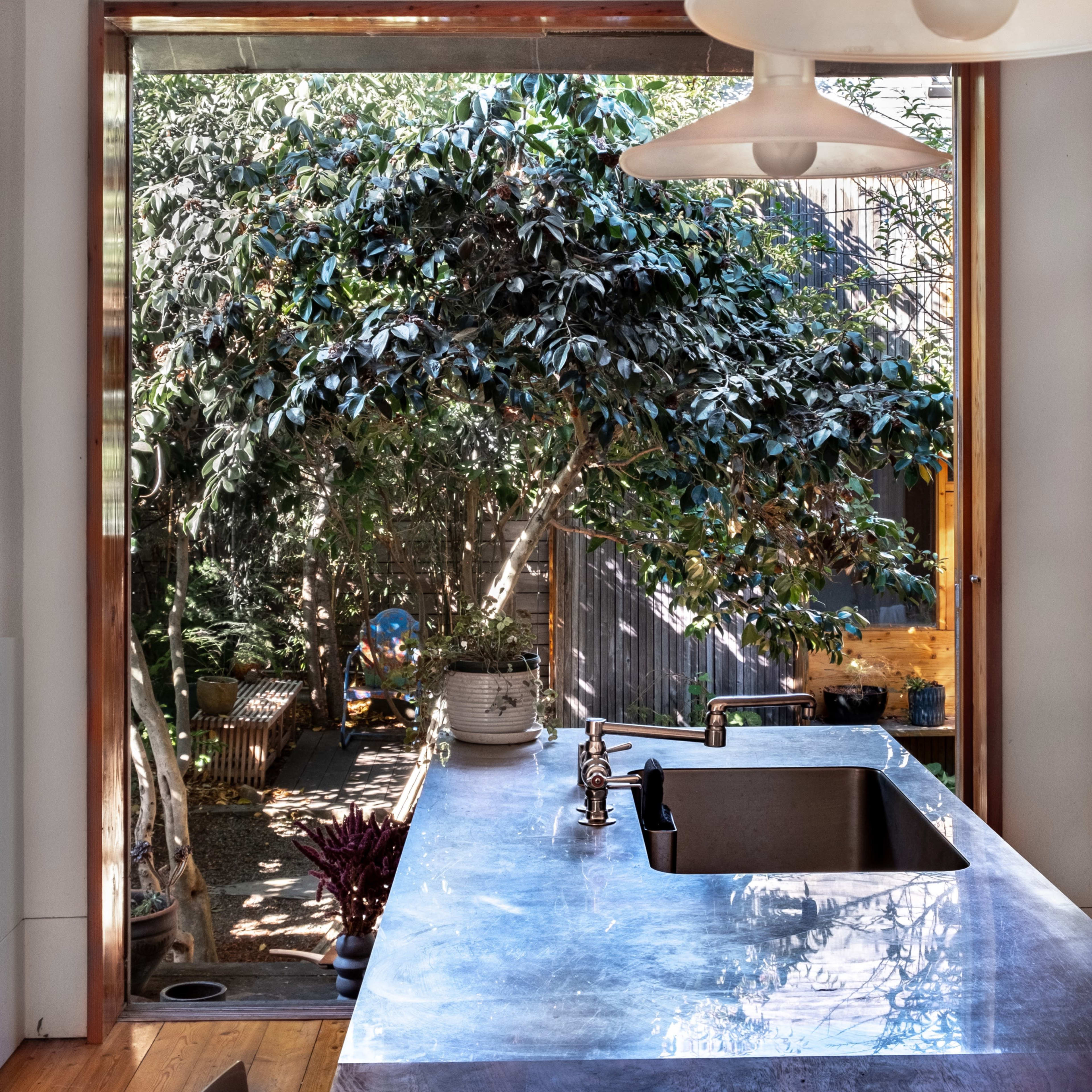 A modern kitchen with a polished countertop overlooks a lush garden through a large open window.