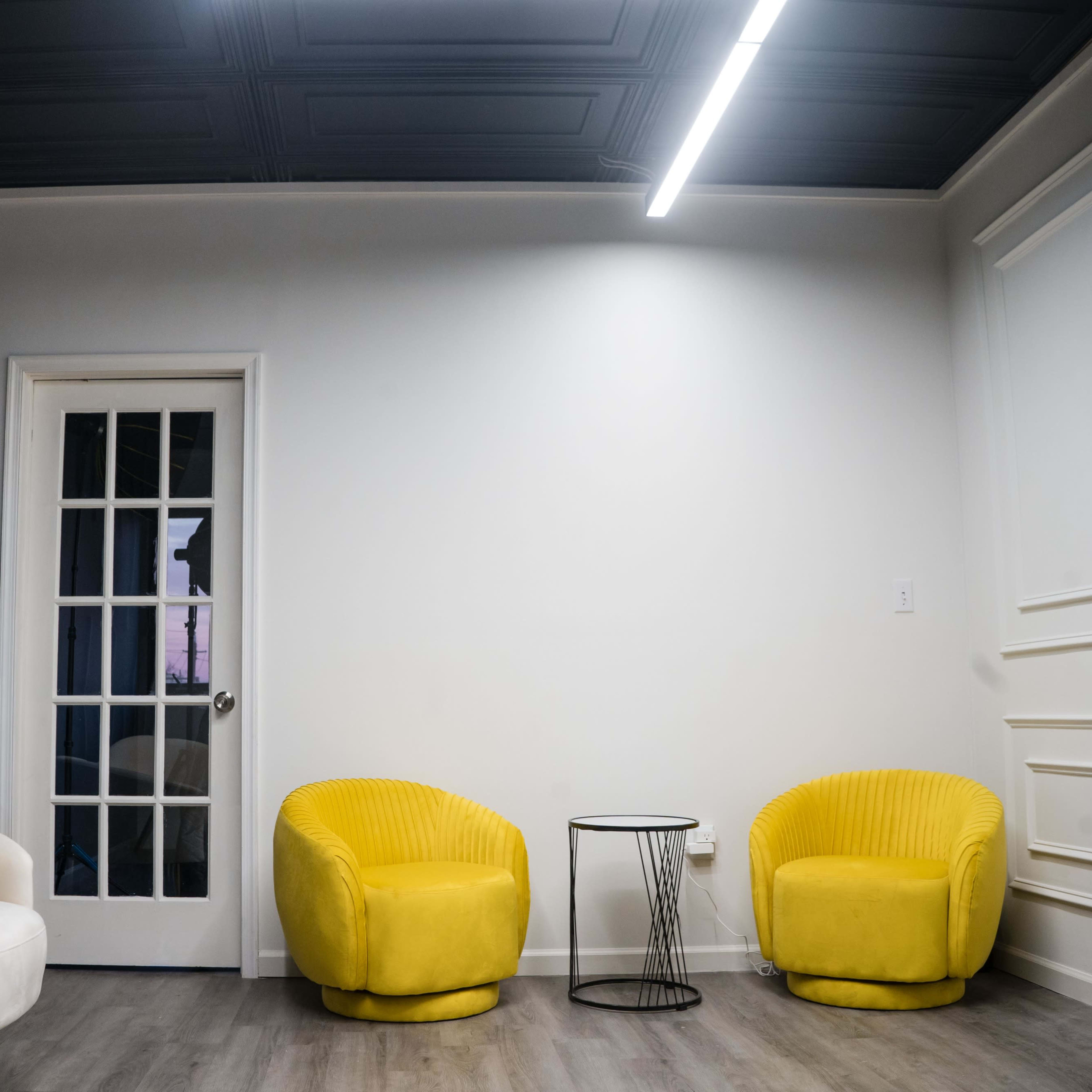 A spacious room features a white couch, two yellow armchairs, a small black side table, and a door with glass panels.