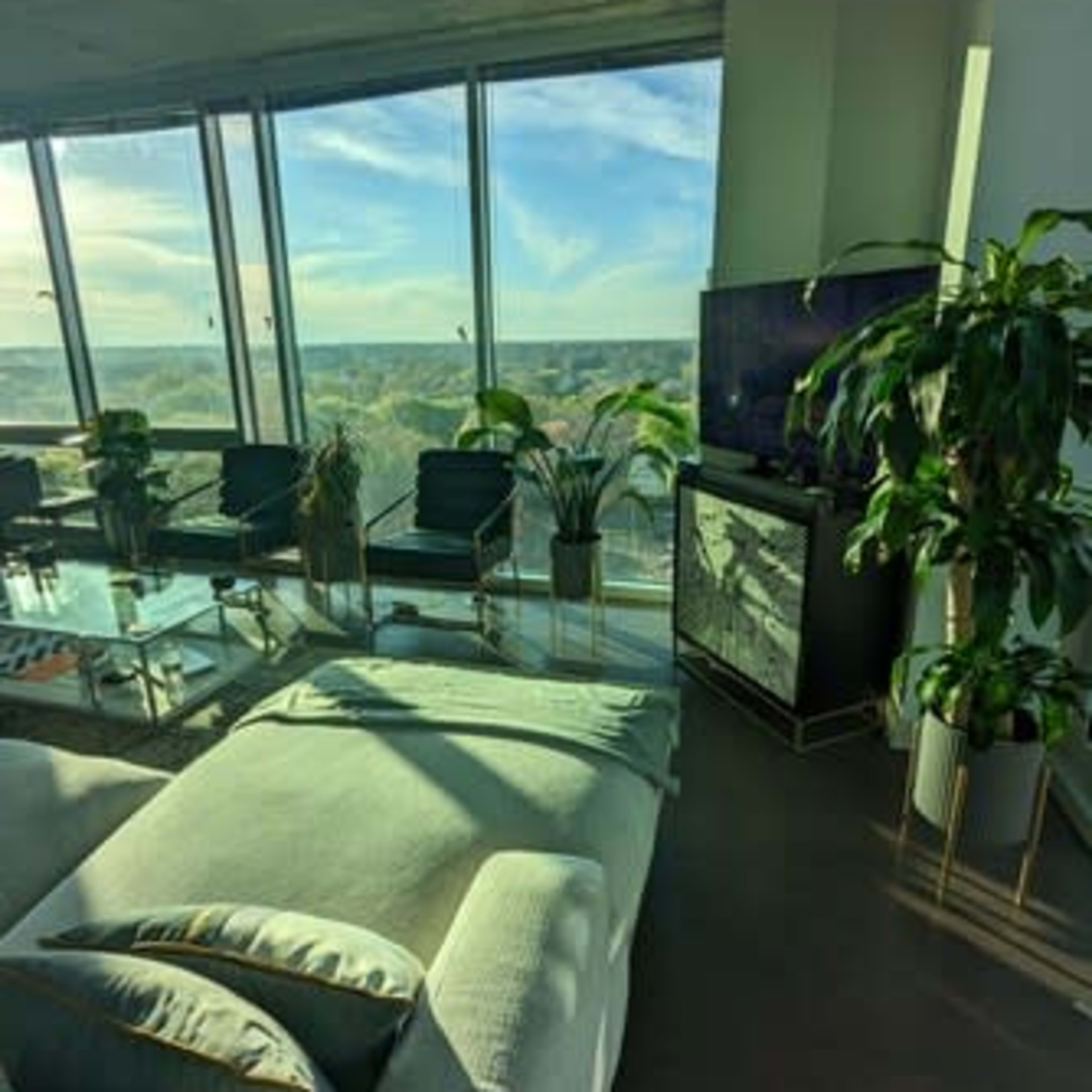 A modern living room features a comfortable sofa, glass furniture, and large windows that offer a view of the landscape outside.
