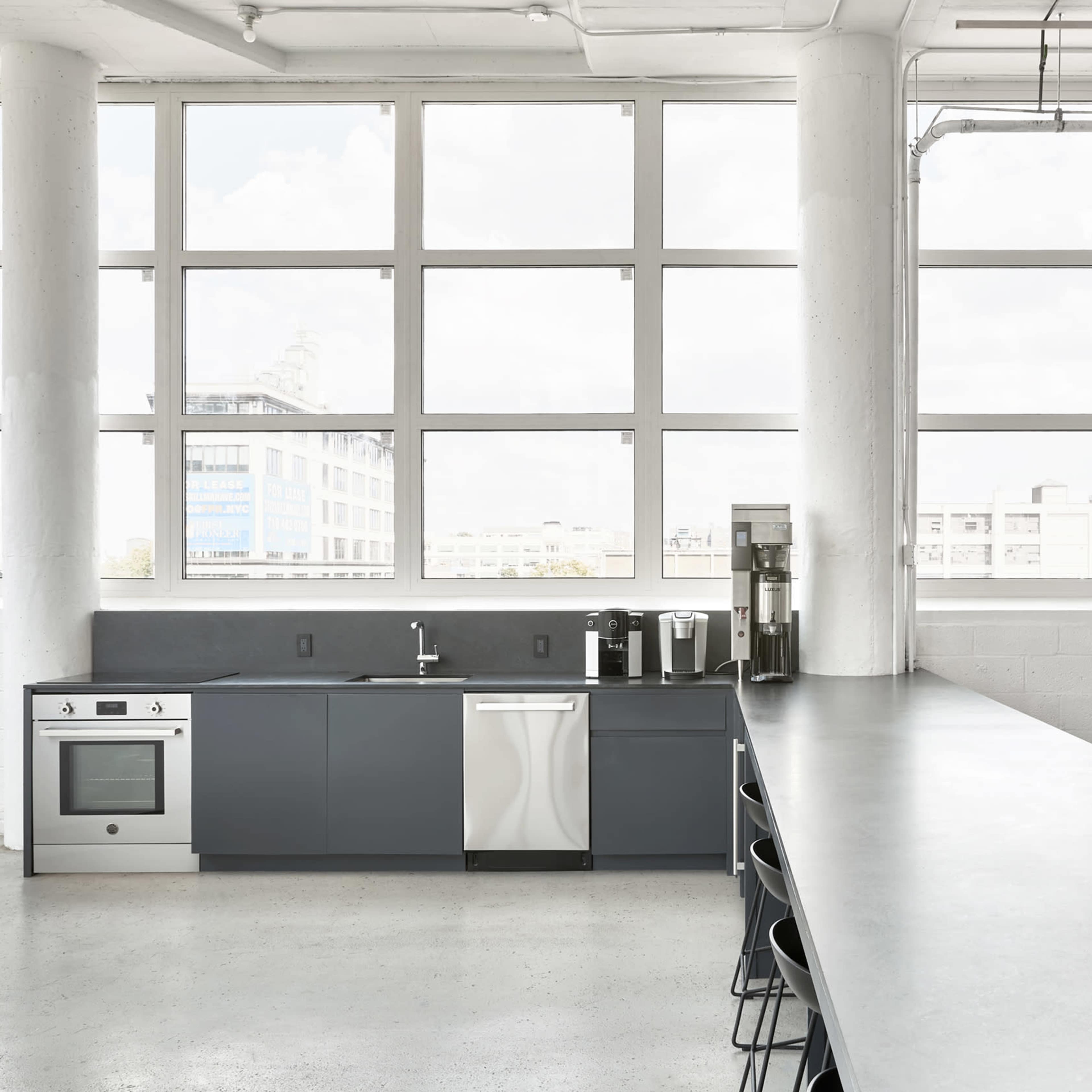 A modern kitchen features grey cabinetry, stainless steel appliances, and large windows that provide ample natural light.