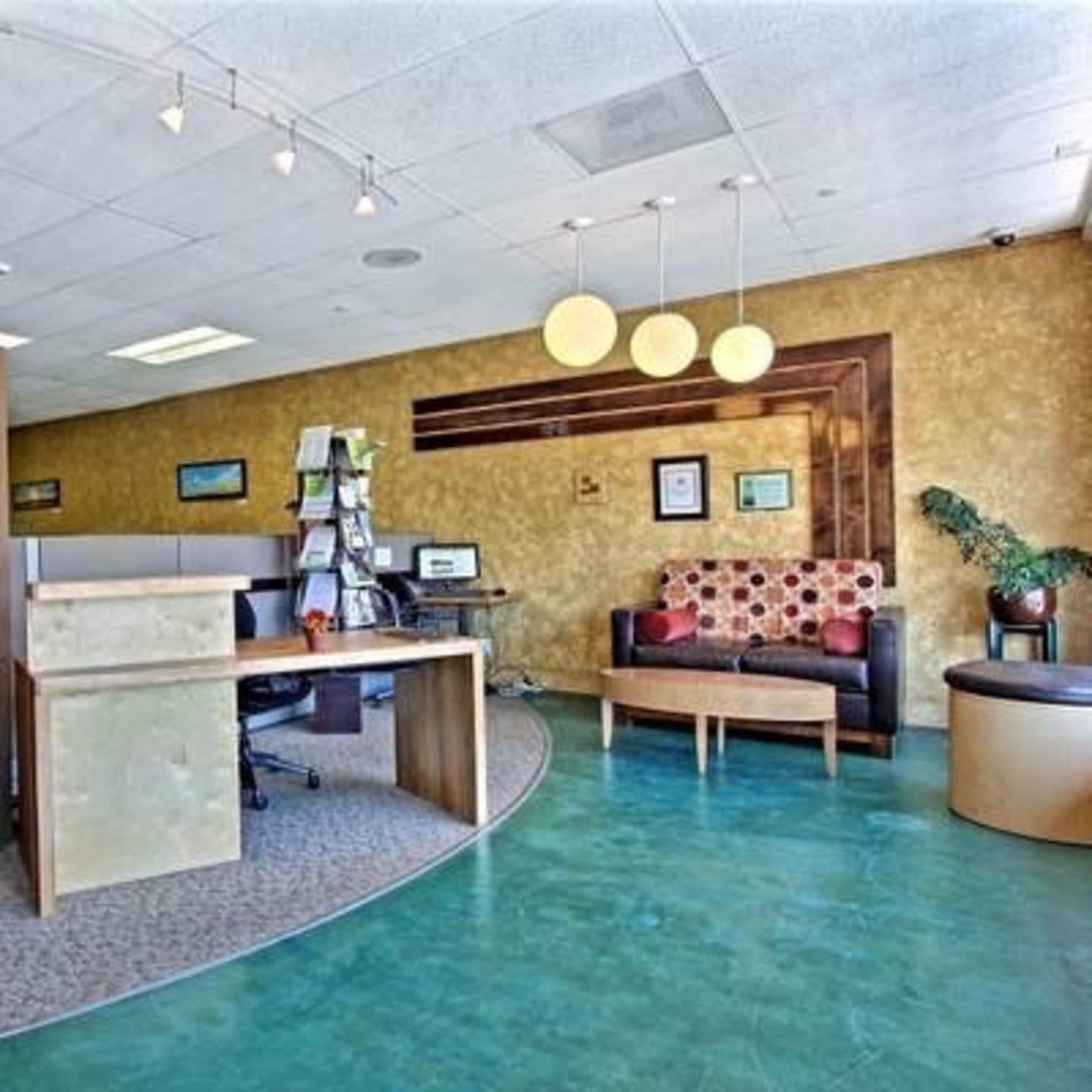 An office reception area with a circular layout, featuring a front desk, a seating area with a patterned couch, and a potted plant.