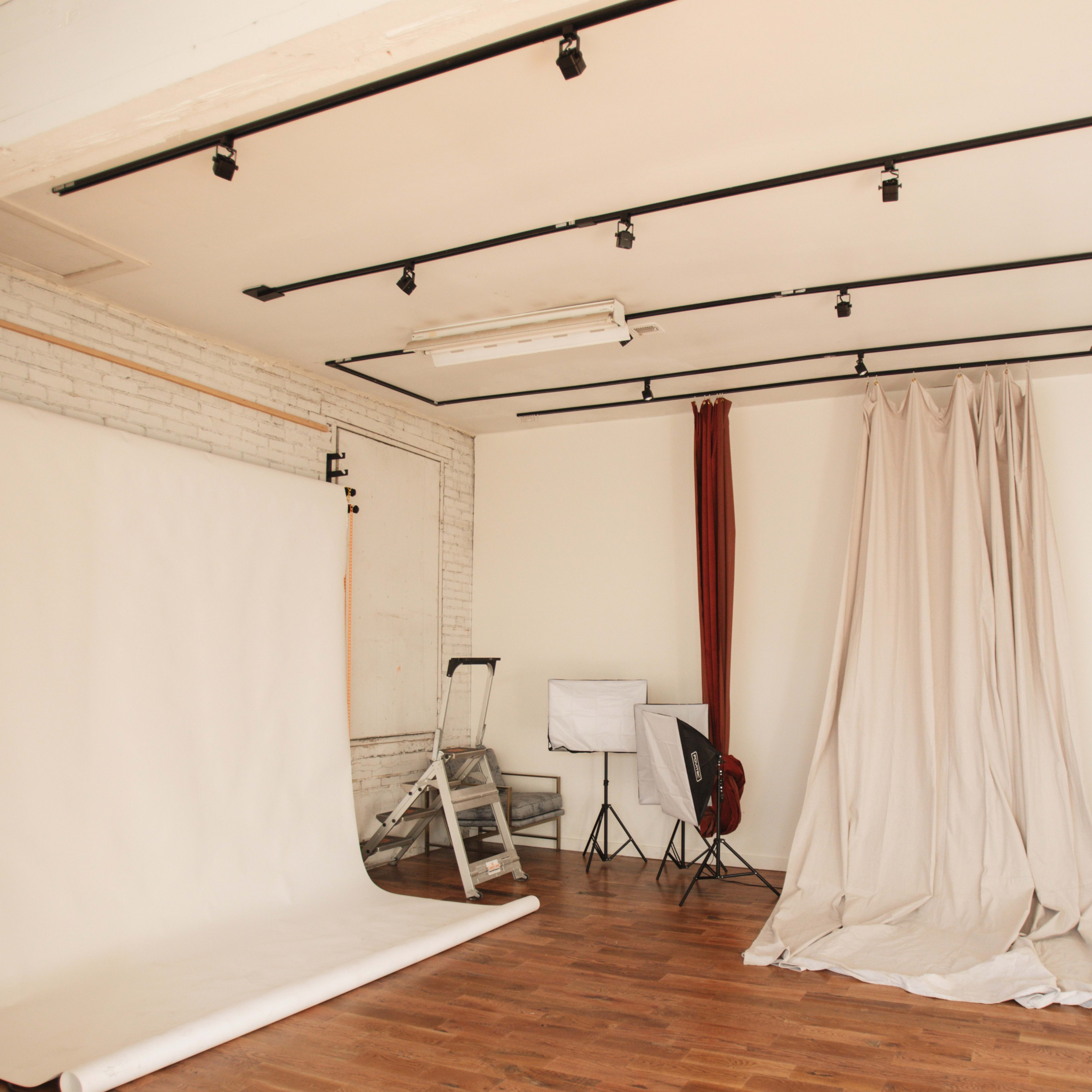 A photography studio with a backdrop, lighting equipment, and neutral-colored drapes.