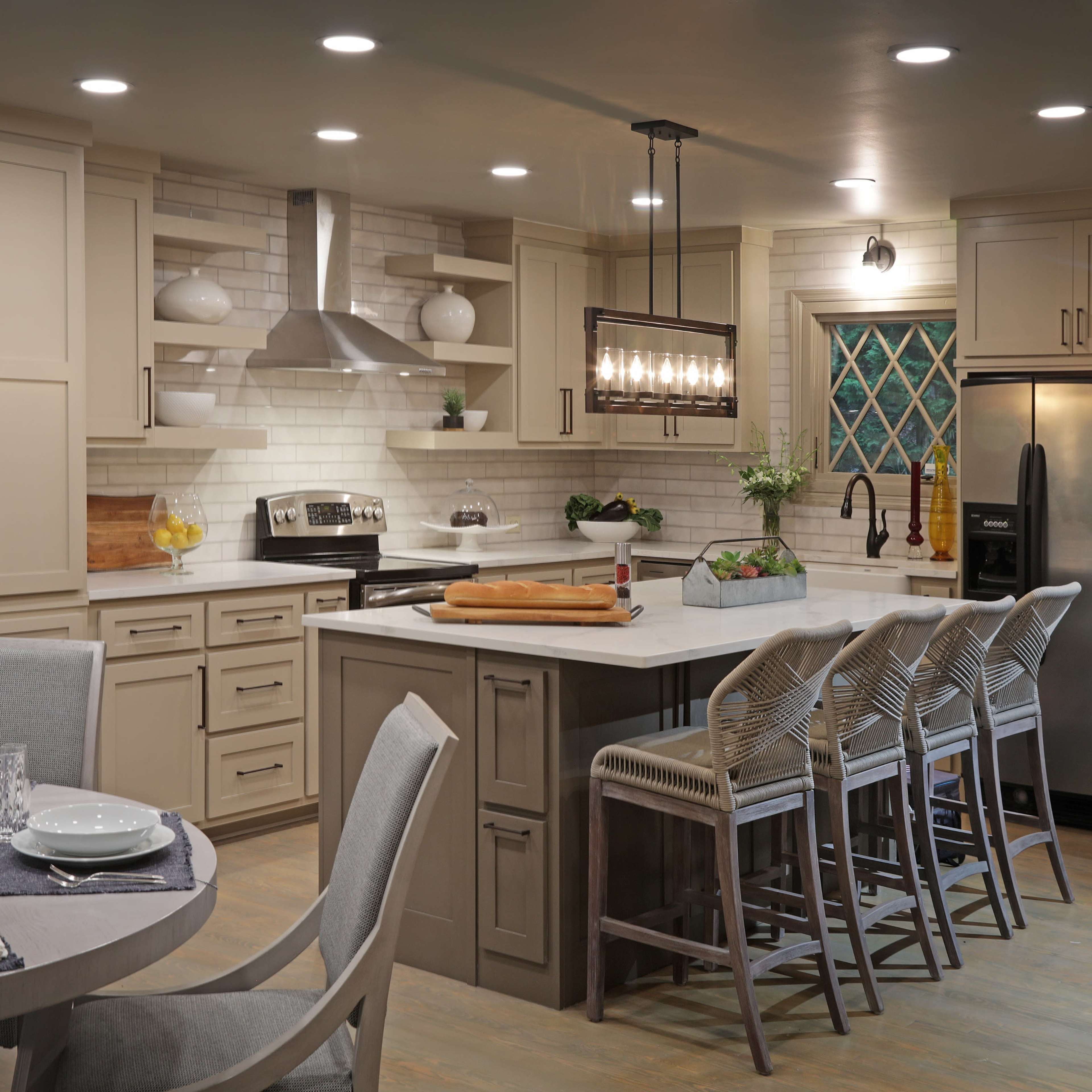 A modern kitchen features beige cabinetry, a large island with bar stools, and a dining area with a round table set for a meal.