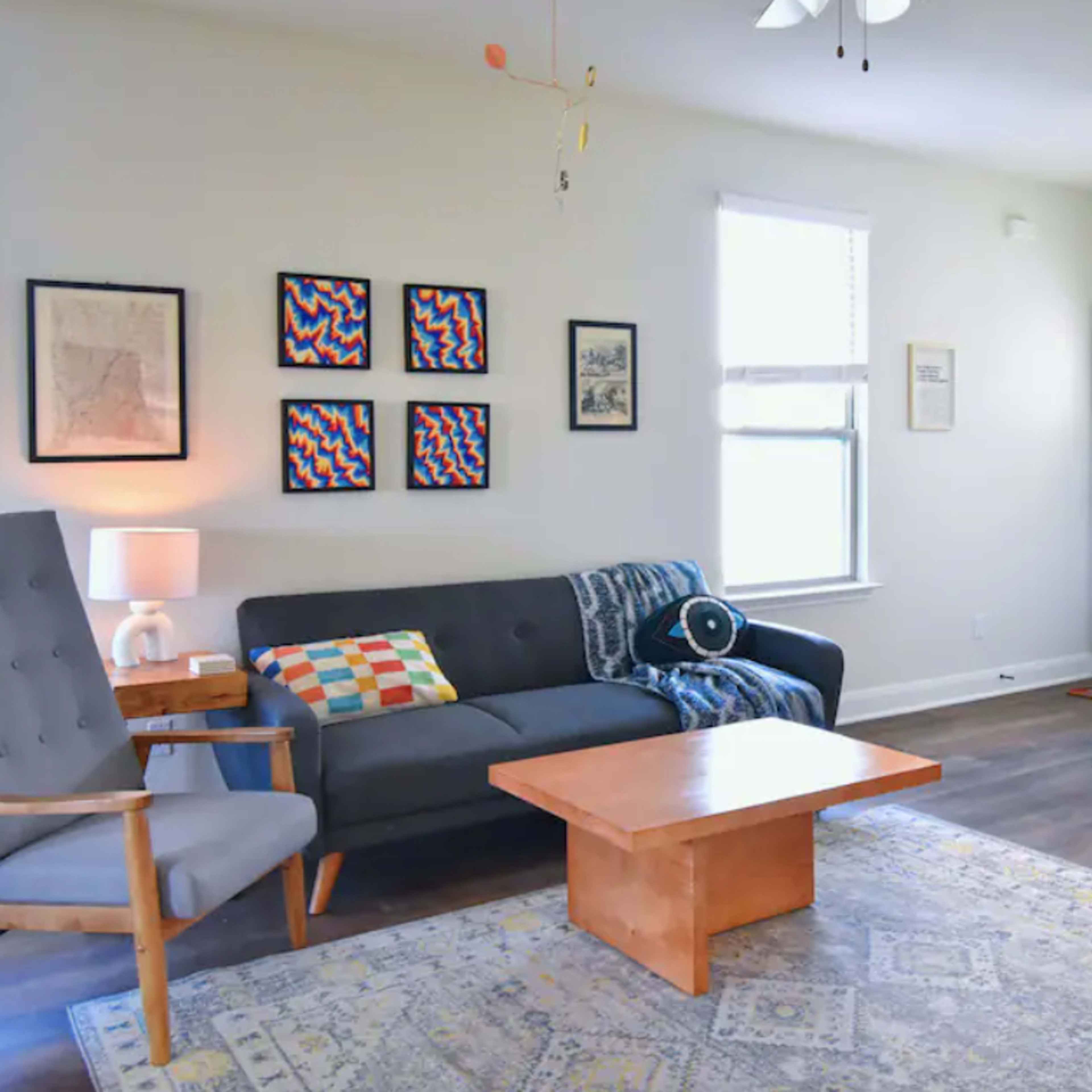 A modern living room featuring a gray sofa, two armchairs, a coffee table, patterned wall art, and a side table with a lamp.